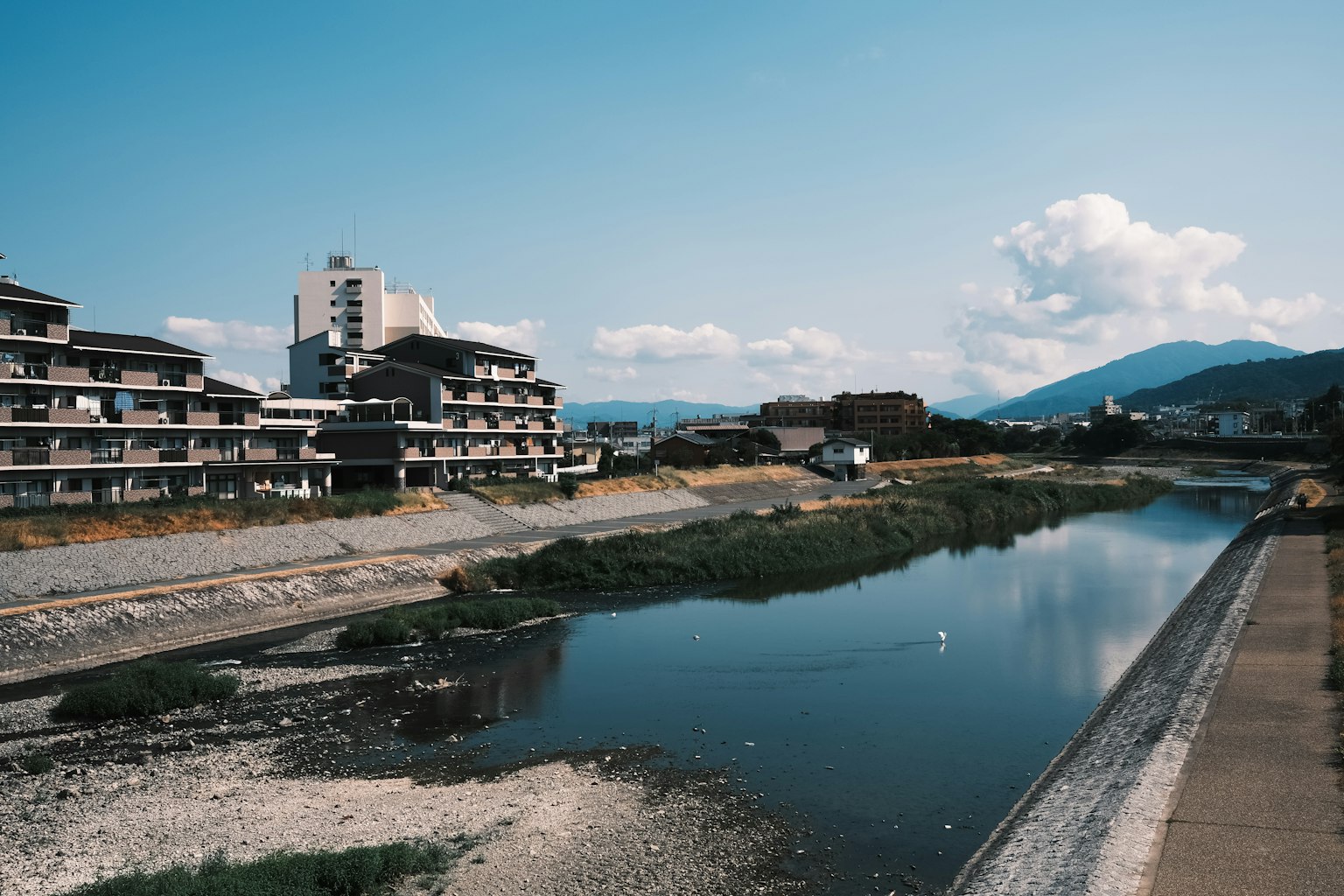 川と建物が見える風景で青い空と山が背景にある