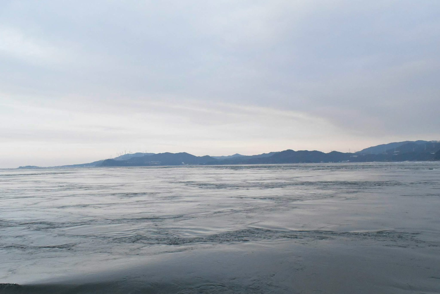 Paysage maritime calme avec des montagnes lointaines sous un ciel nuageux
