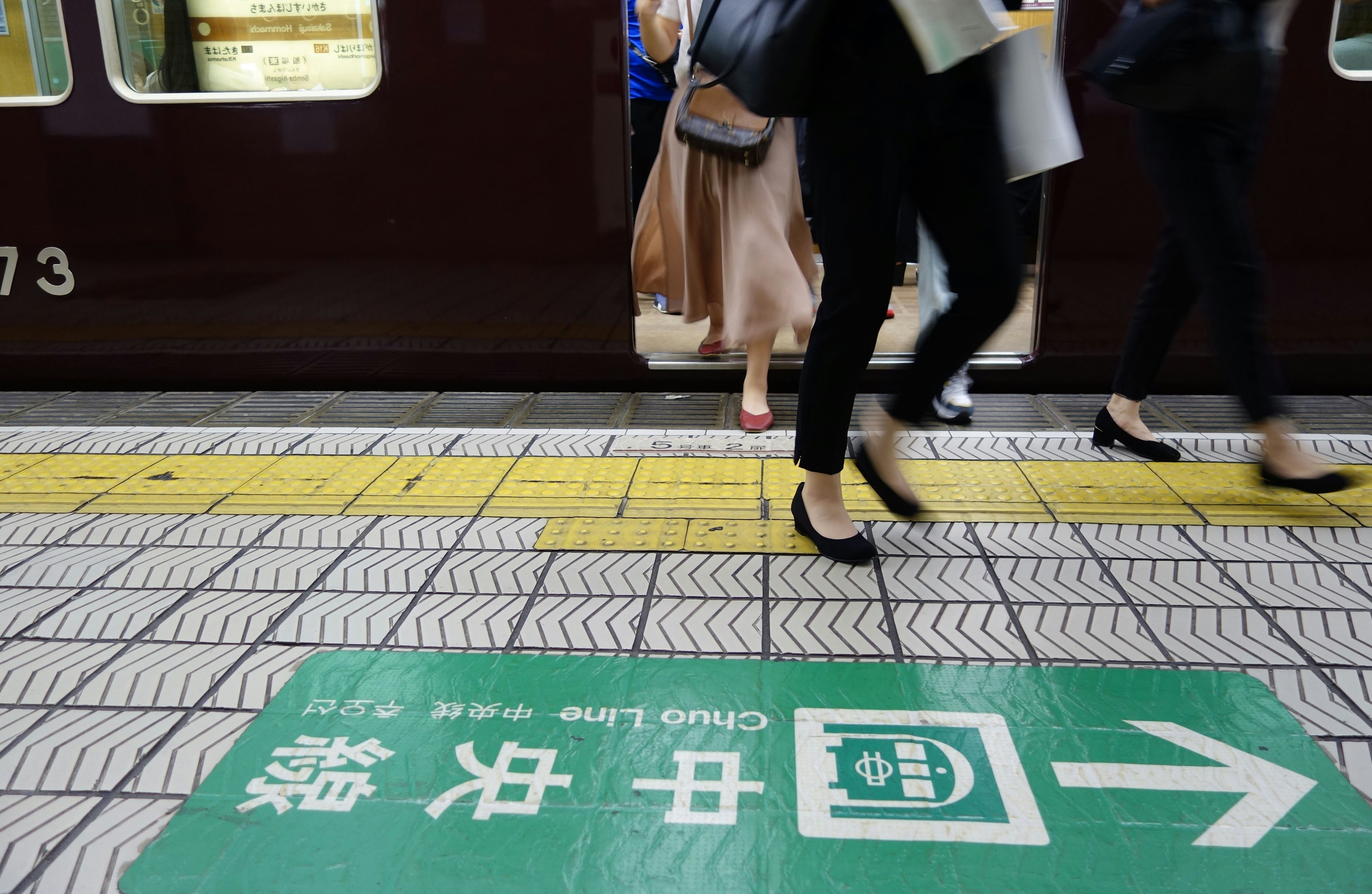 駅のホームで歩く人と緑の案内標識のある線路側の床