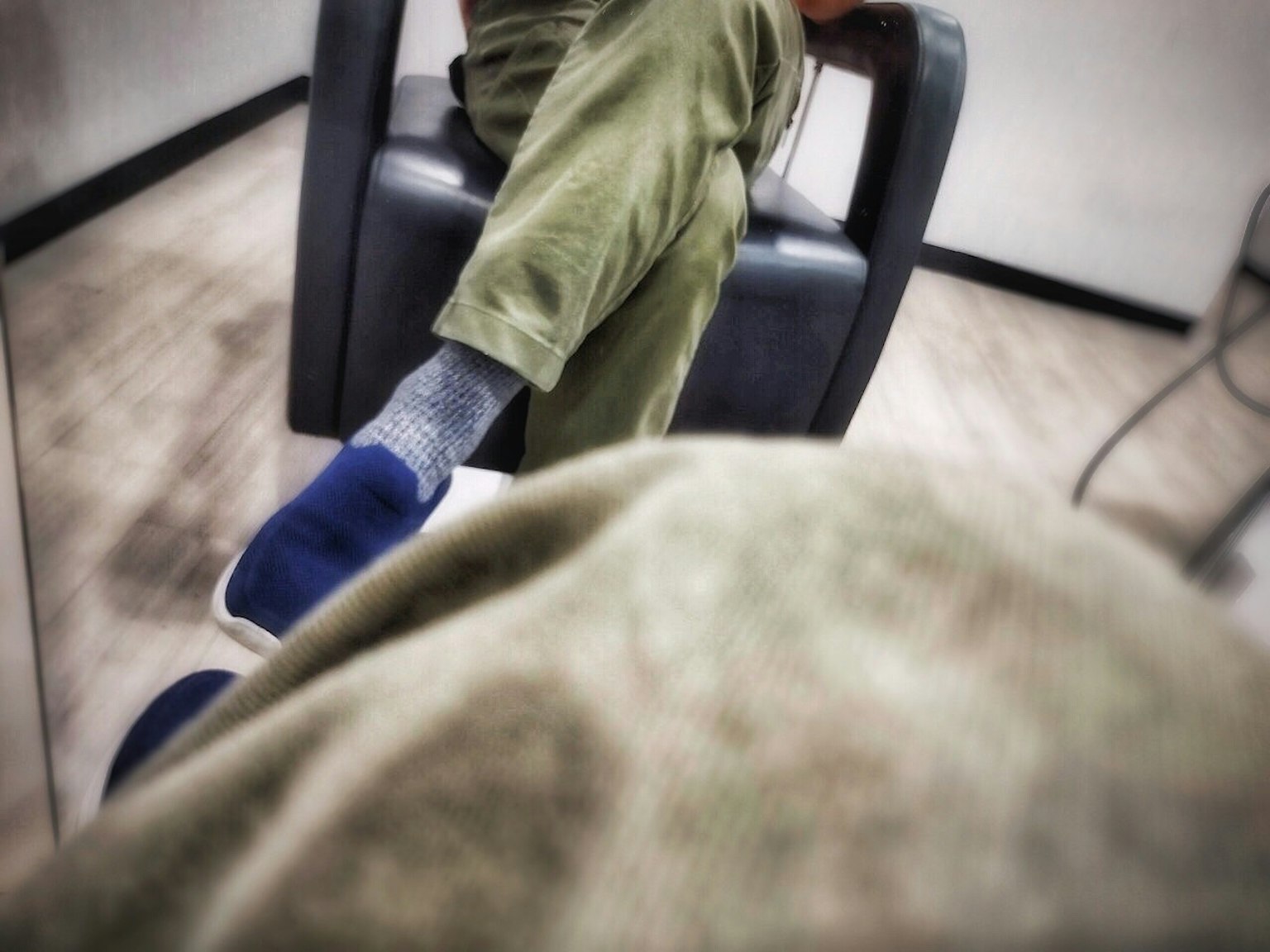 Close-up of a person's feet in a chair featuring blue sneakers and green pants