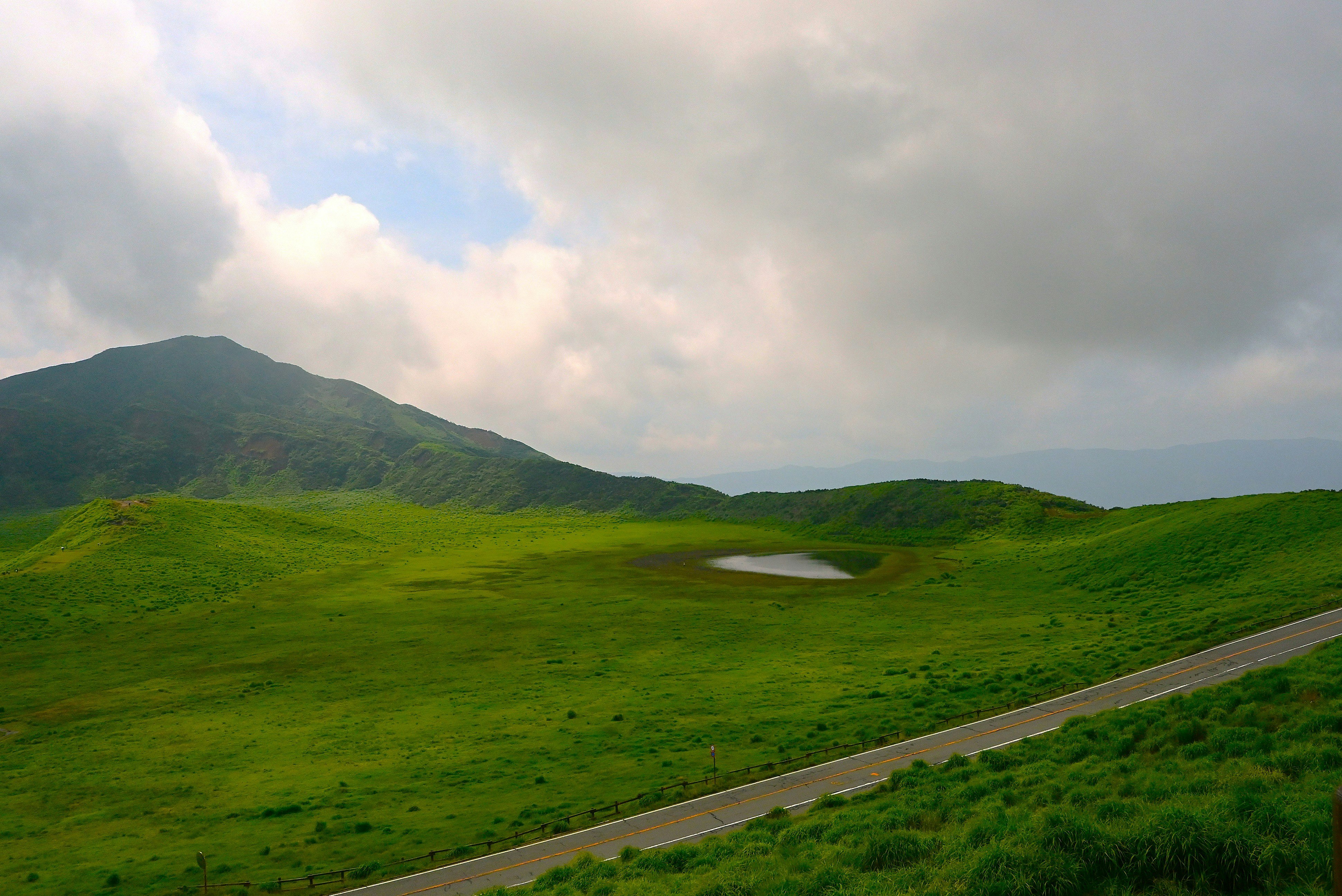阿蘇の草原と山並み、雲の下の道