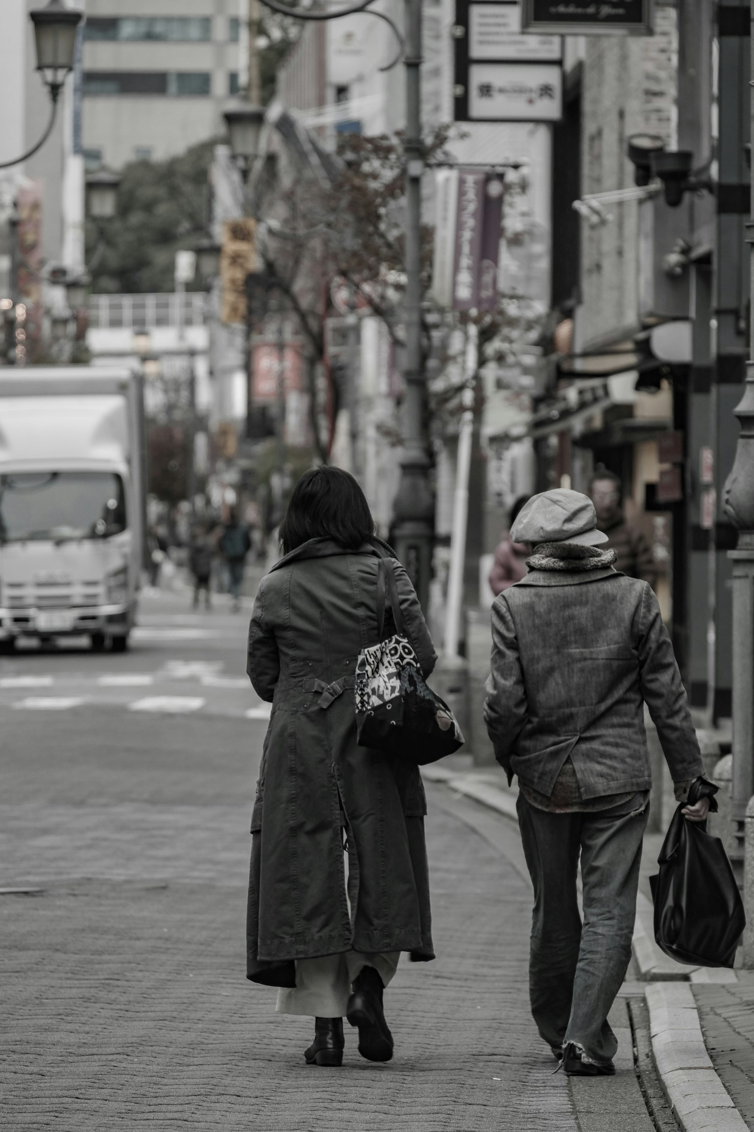 兩位穿著外套的女性走在街上，附近停著一輛卡車