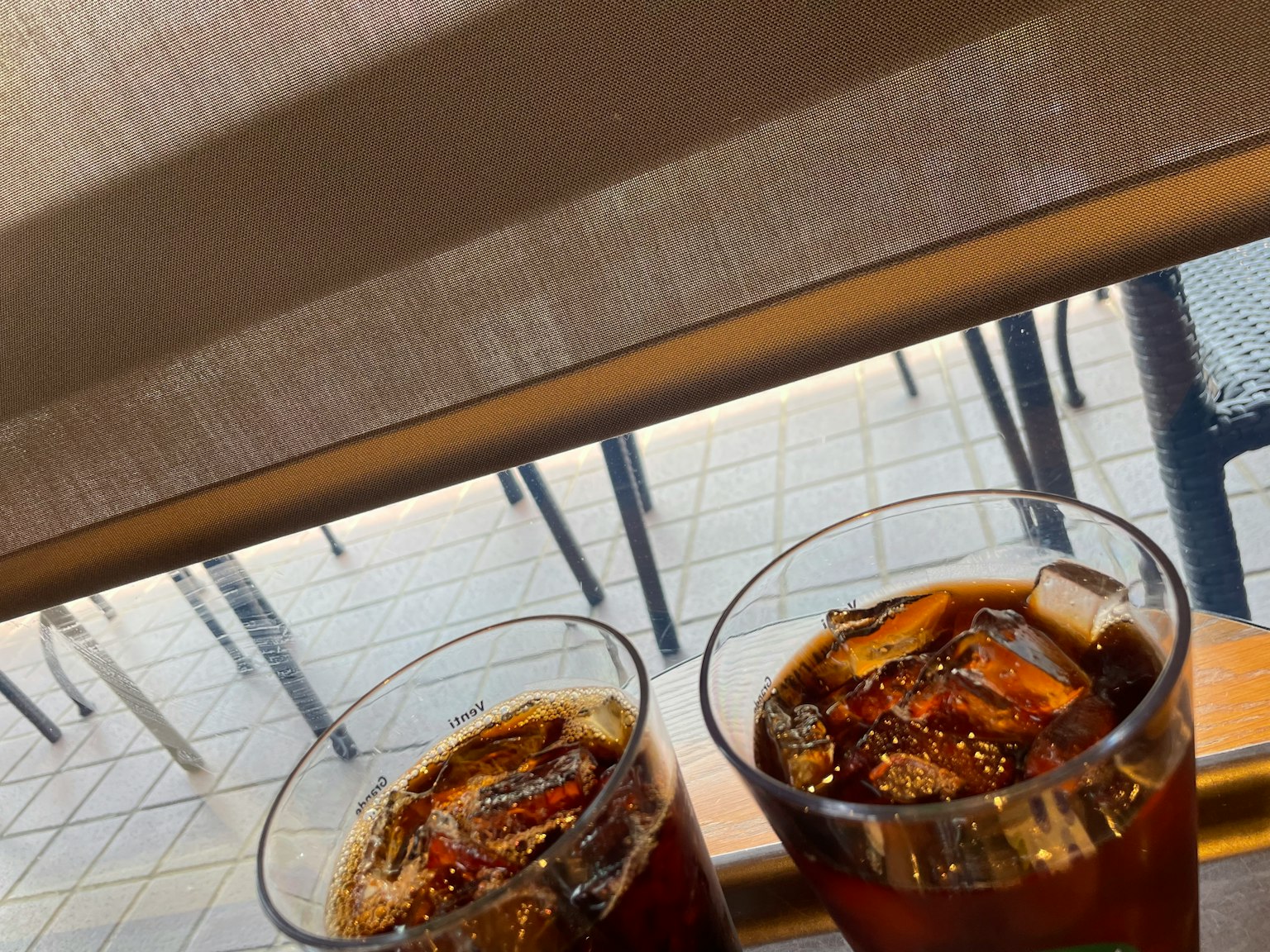 창턱에 놓인 두 잔의 아이스 음료와 보이는 야외 좌석