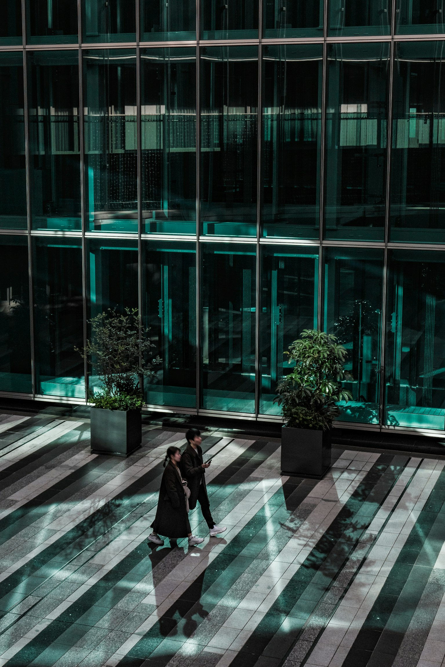 สองคนเดินอยู่หน้าตึกกระจกที่มีต้นไม้เขียวขจี