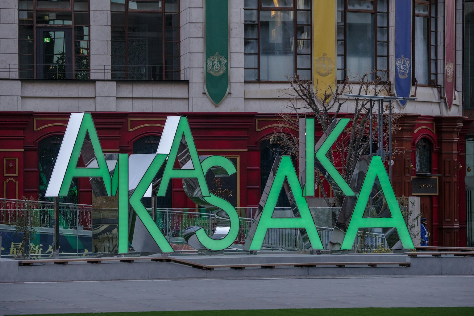 Chữ cái lớn màu xanh lá cây đánh vần 'AKASAKA' với nền thành phố