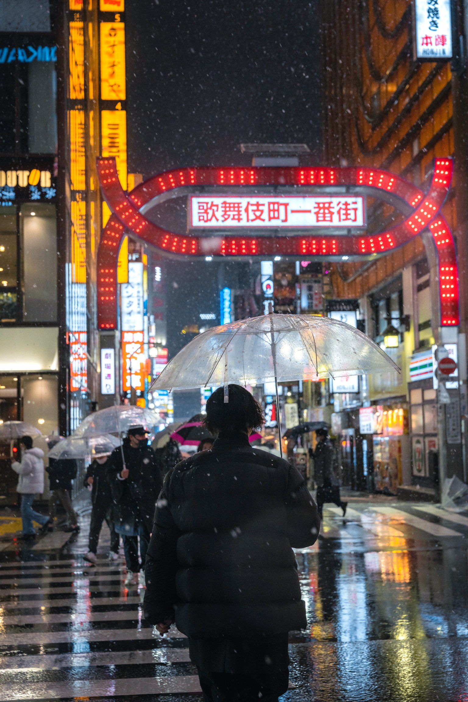 Una escena de calle animada por la noche con nieve cayendo y un letrero en arco rojo prominente