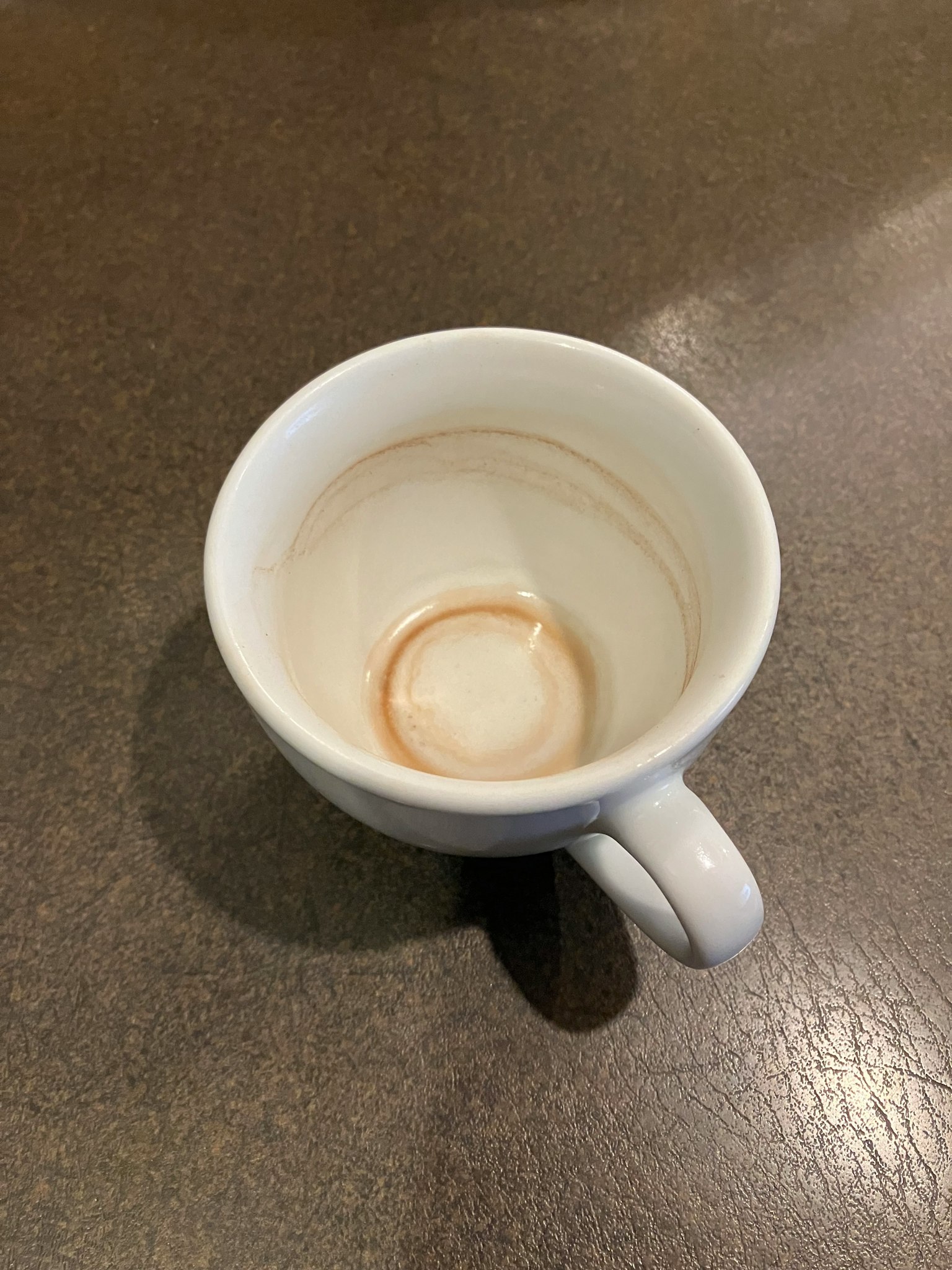 Cangkir putih dengan noda kopi berbentuk cincin di bagian bawah