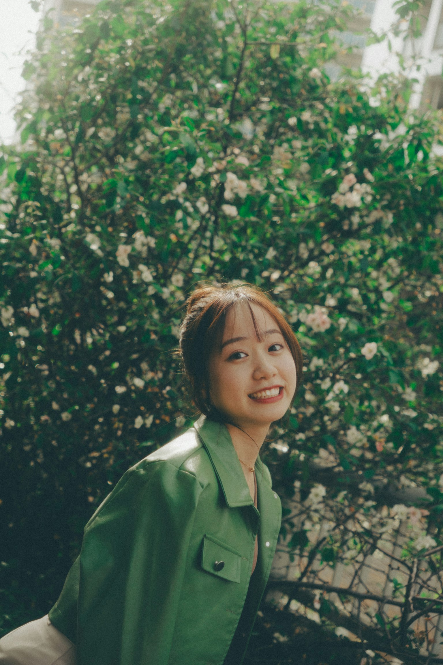 Mujer con chaqueta verde sonriendo frente a flores