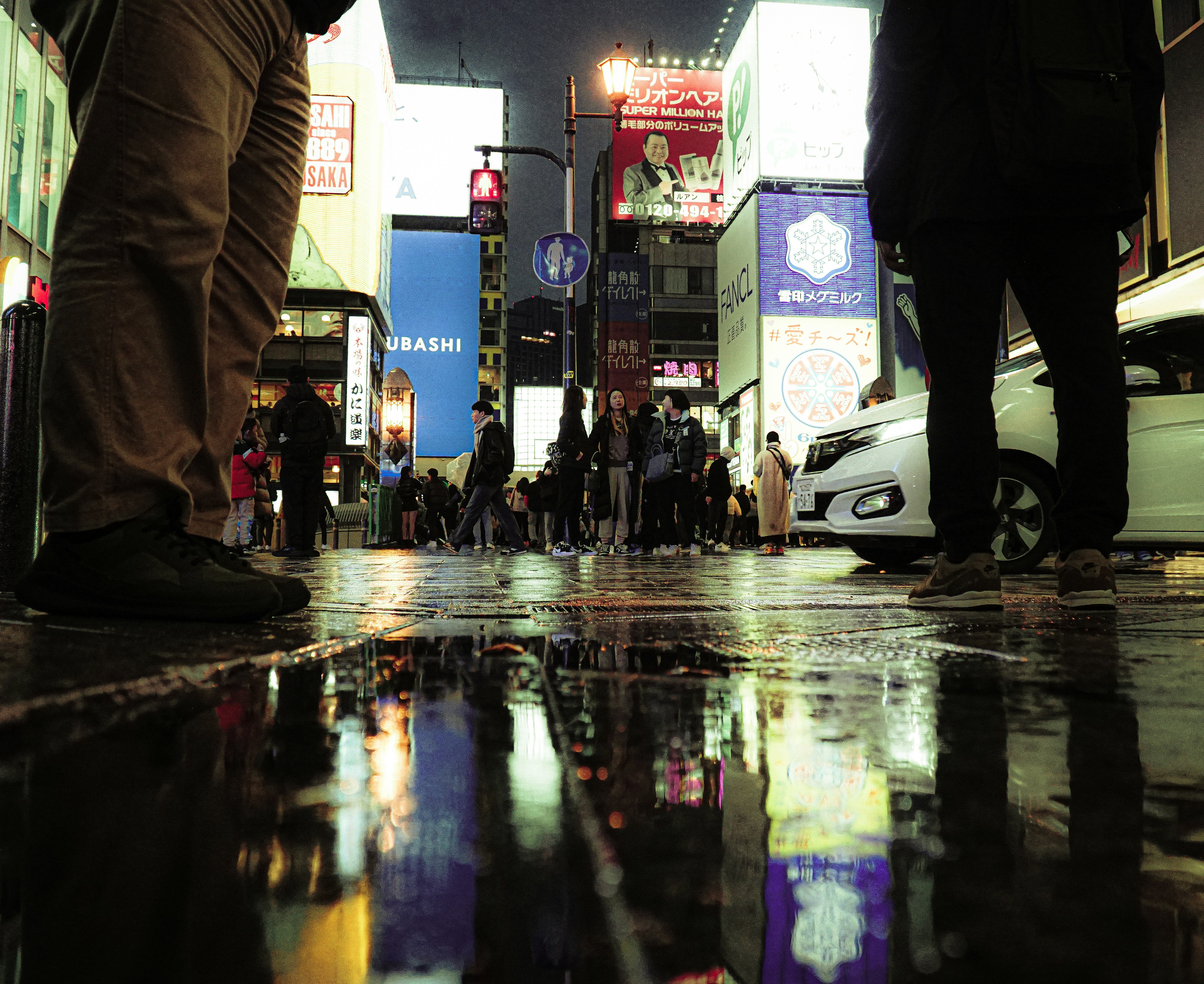 雨上がりの路地で人々と車の行き交う夜の街並み