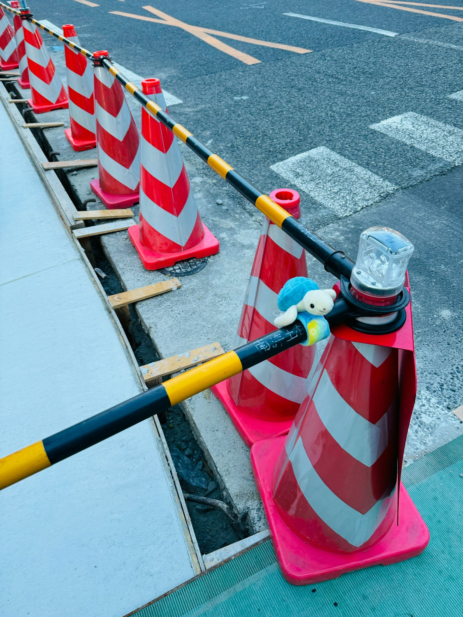 Fila di coni di costruzione rossi e bianchi con un personaggio di peluche blu e una luce trasparente su un cono
