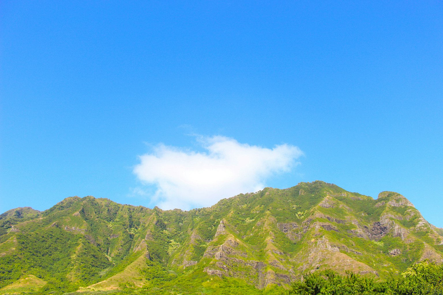 Montagnes verdoyantes sous un ciel bleu avec un nuage blanc
