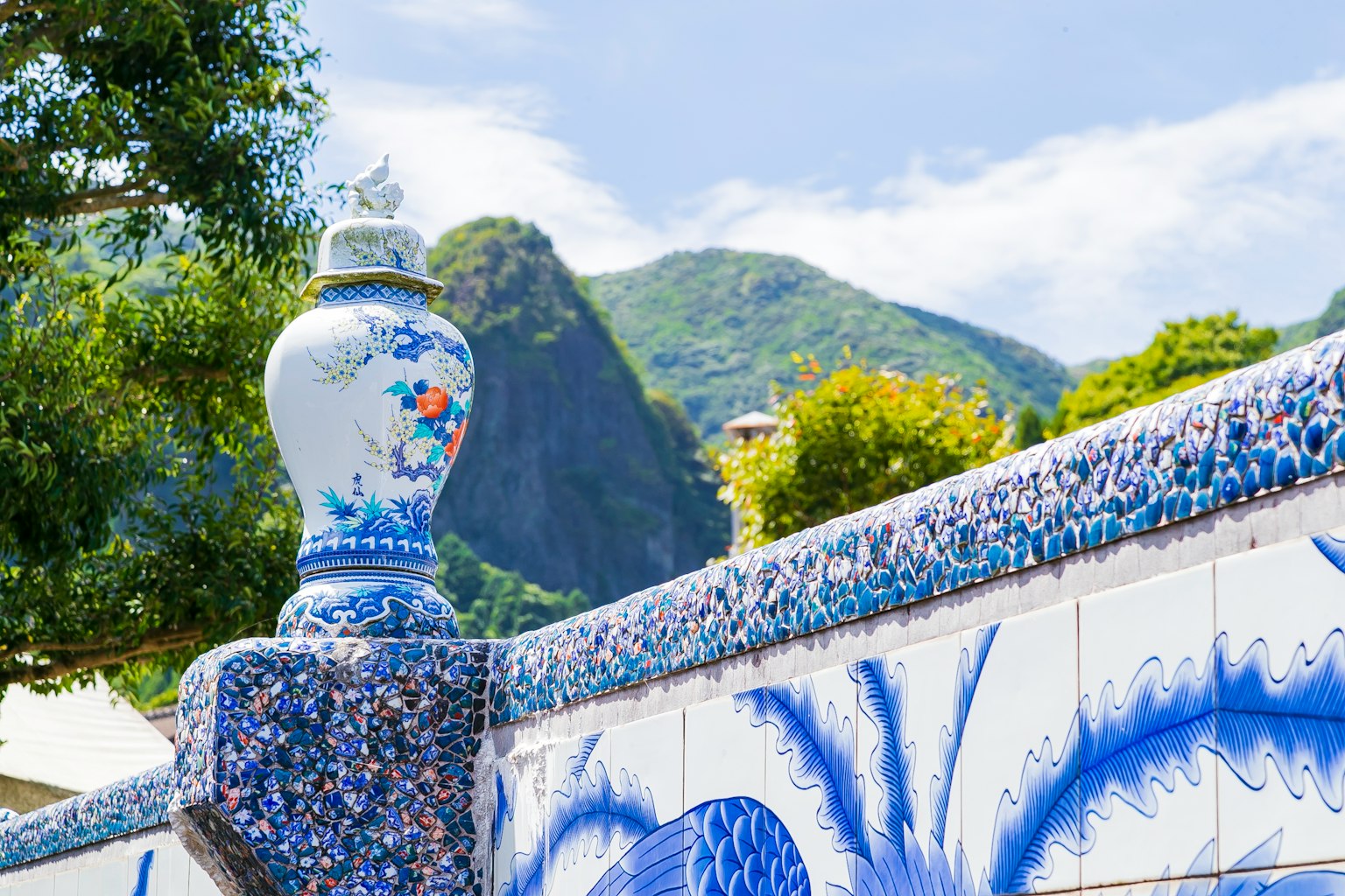Jarrón decorativo azul con un fondo montañoso y vegetación vibrante