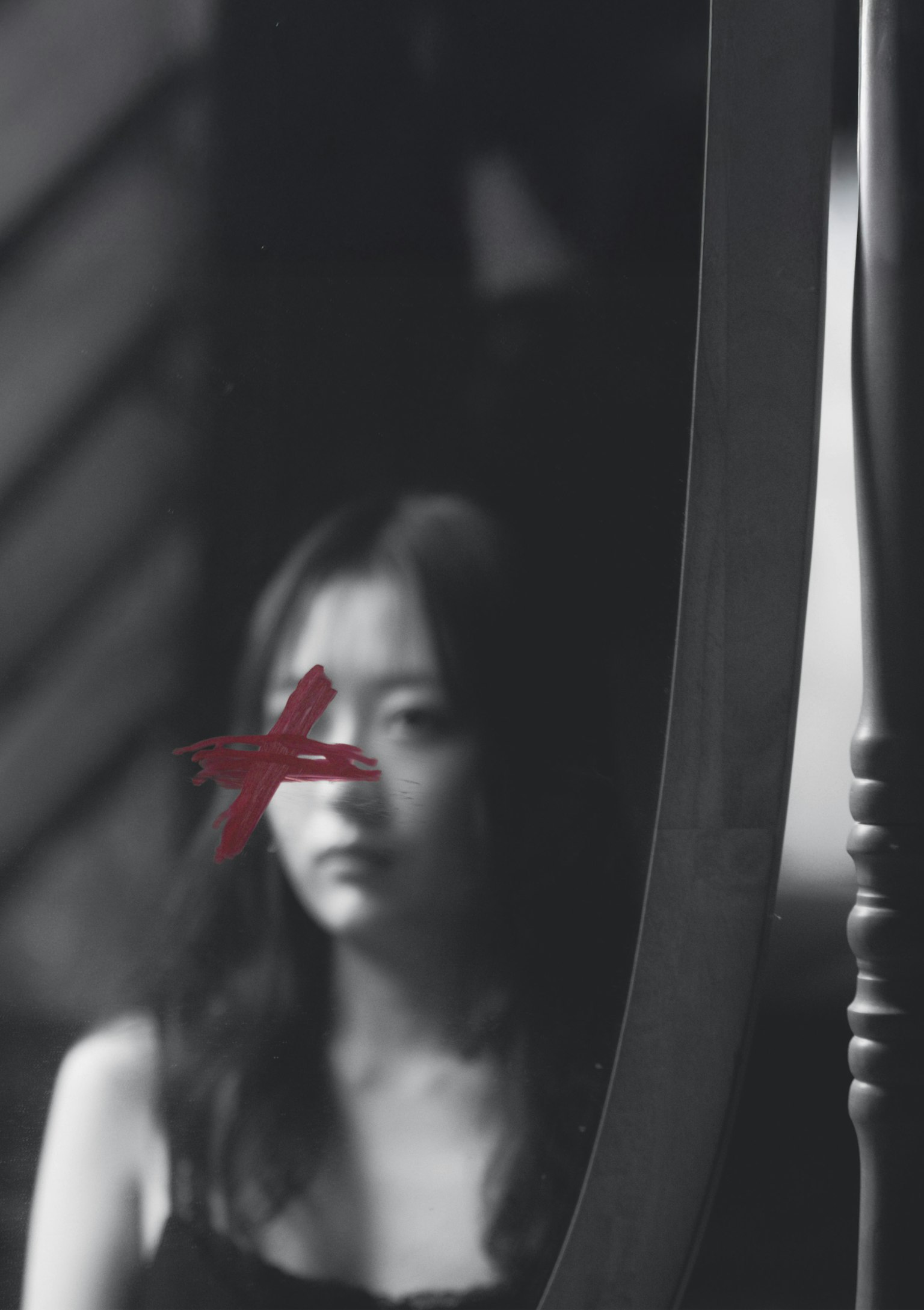 Foto in bianco e nero di una donna davanti a uno specchio con una croce rossa sul viso