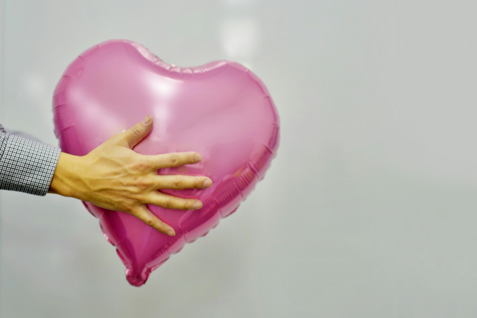 Tangan memegang balon berbentuk hati berwarna pink
