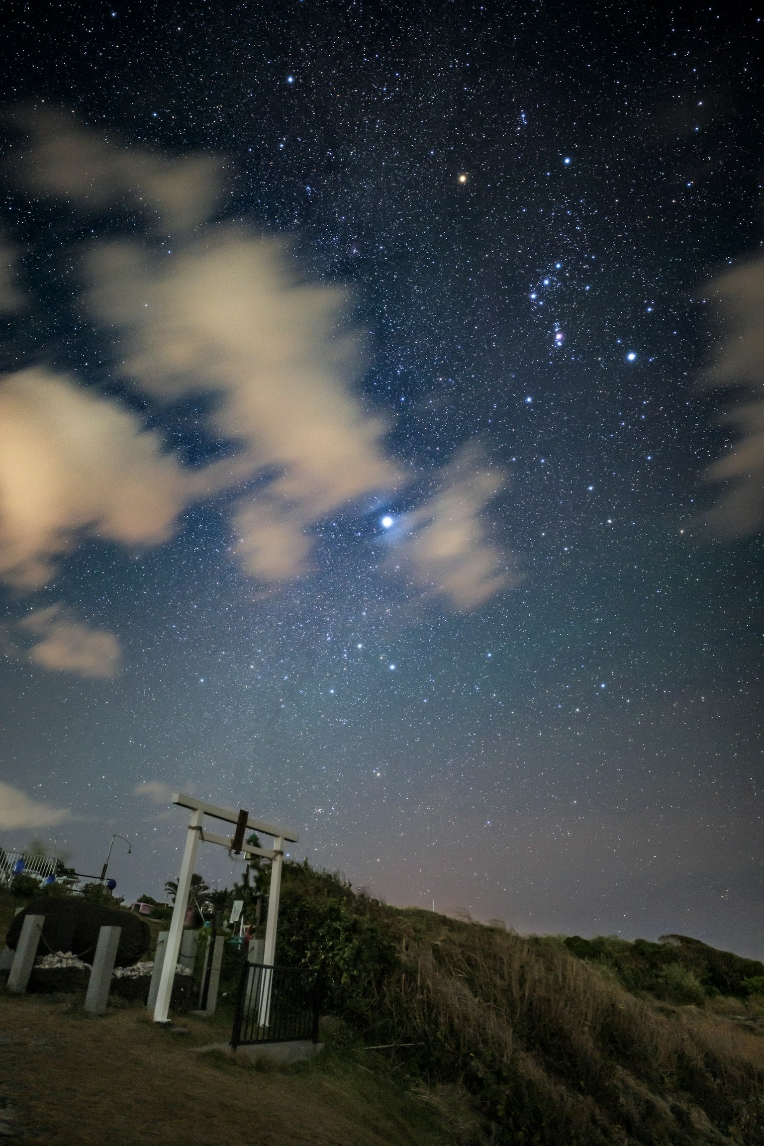 Night sky filled with stars and clouds featuring objects on the ground