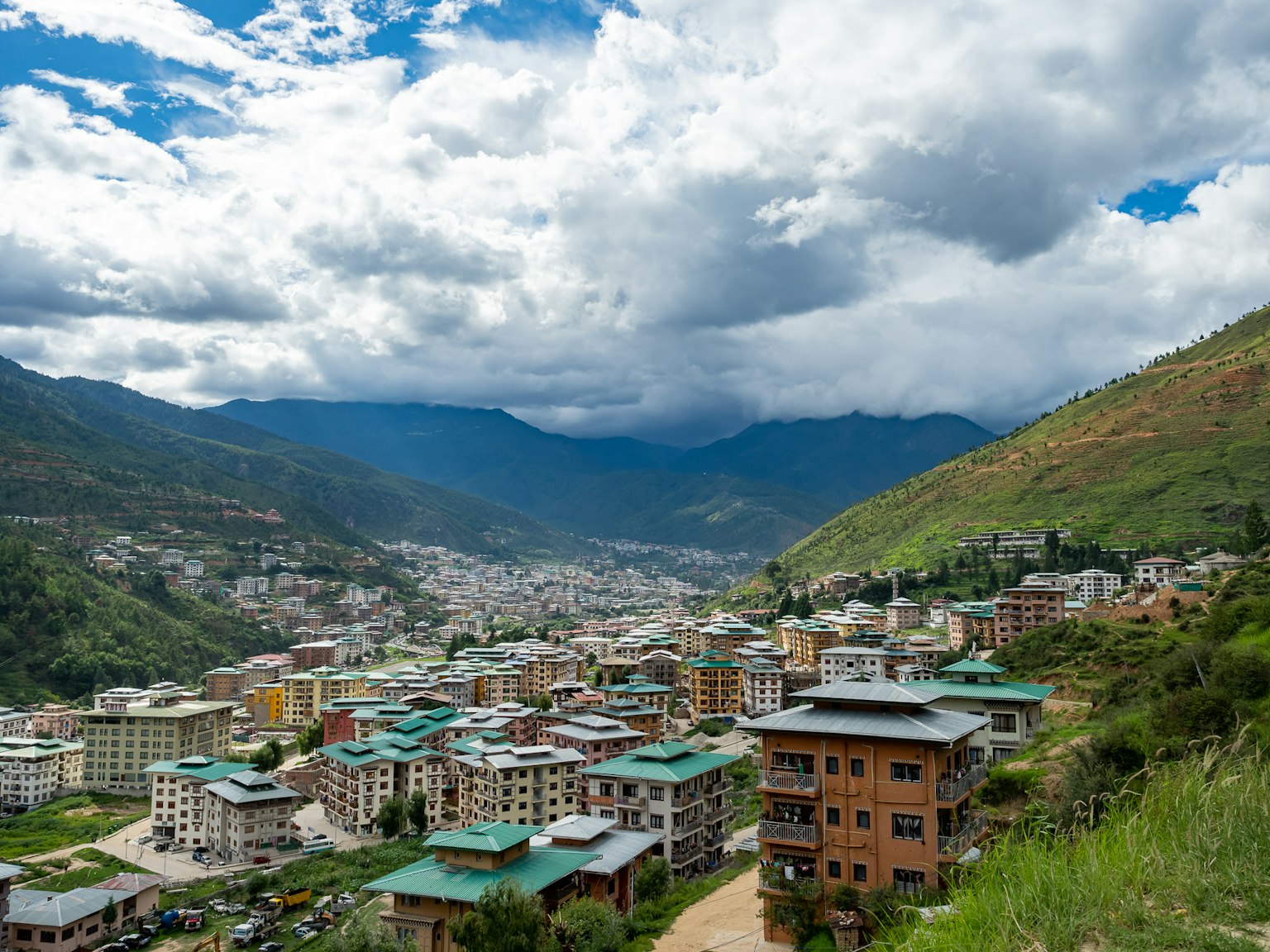 Paysage urbain entouré de collines vertes avec ciel bleu et nuages blancs