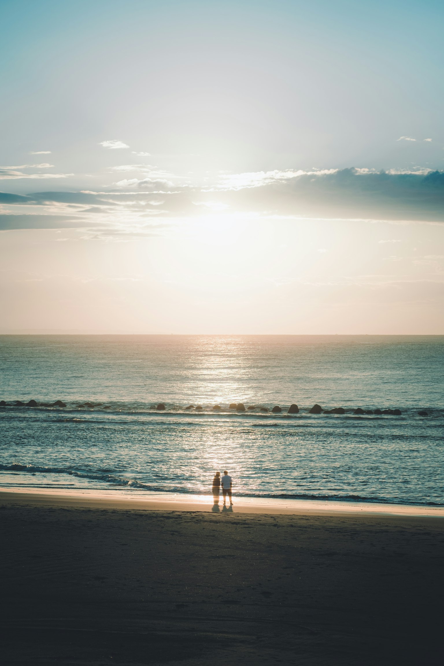 Silhouette di due persone in piedi su una spiaggia con un tramonto sullo sfondo