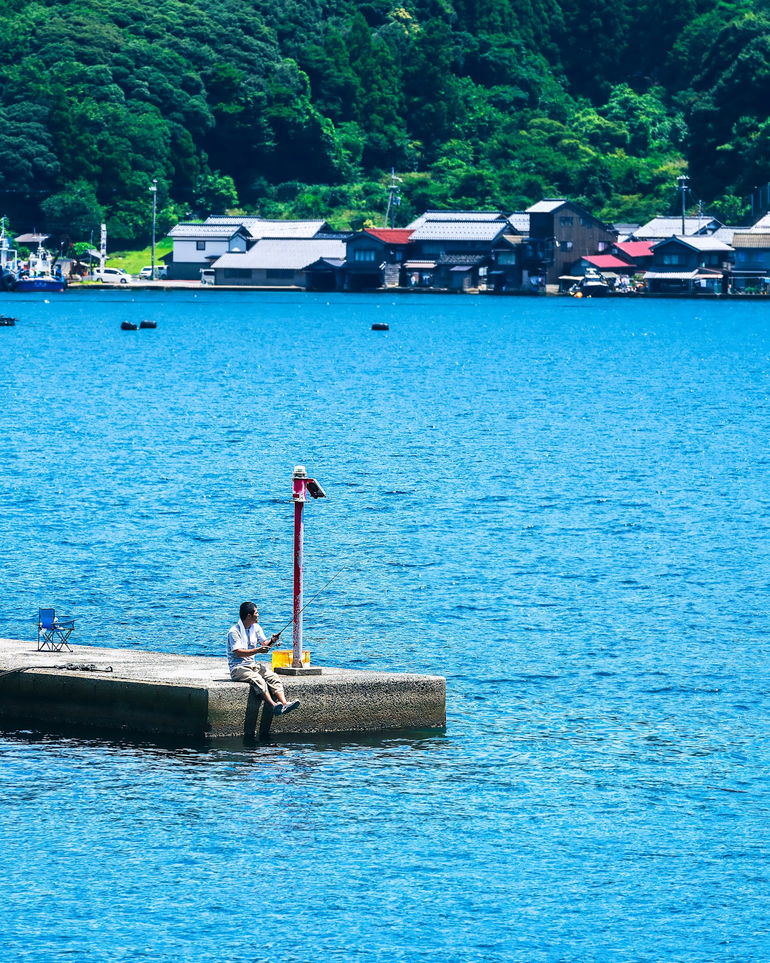 Person sitting on a pier with blue water and small houses in the background