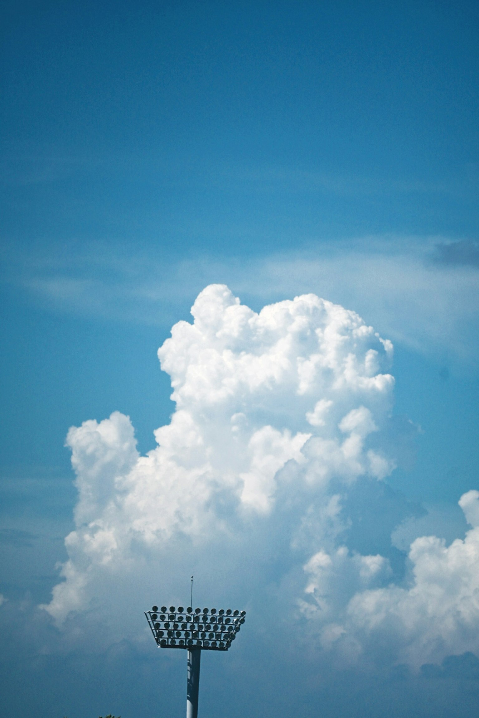 青空に浮かぶ白い雲とスポーツ用照明塔