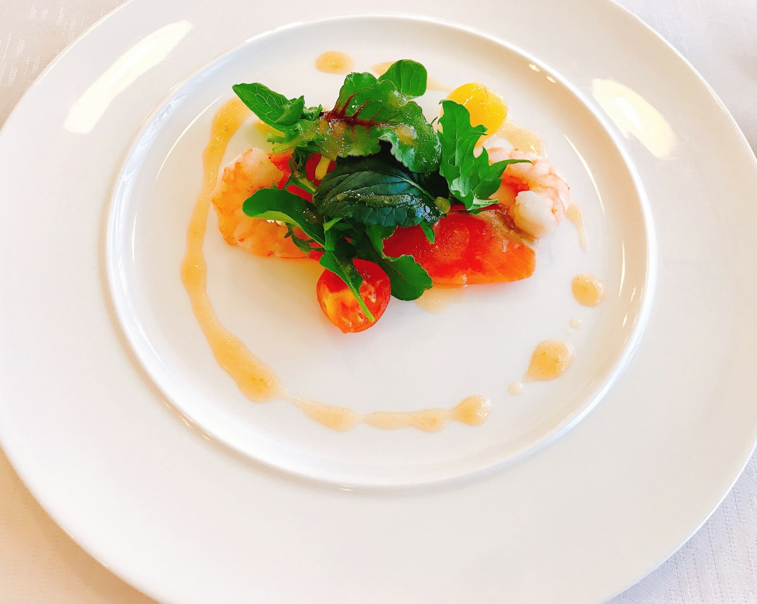 A beautifully plated seafood dish on a white plate topped with fresh tomatoes and herbs