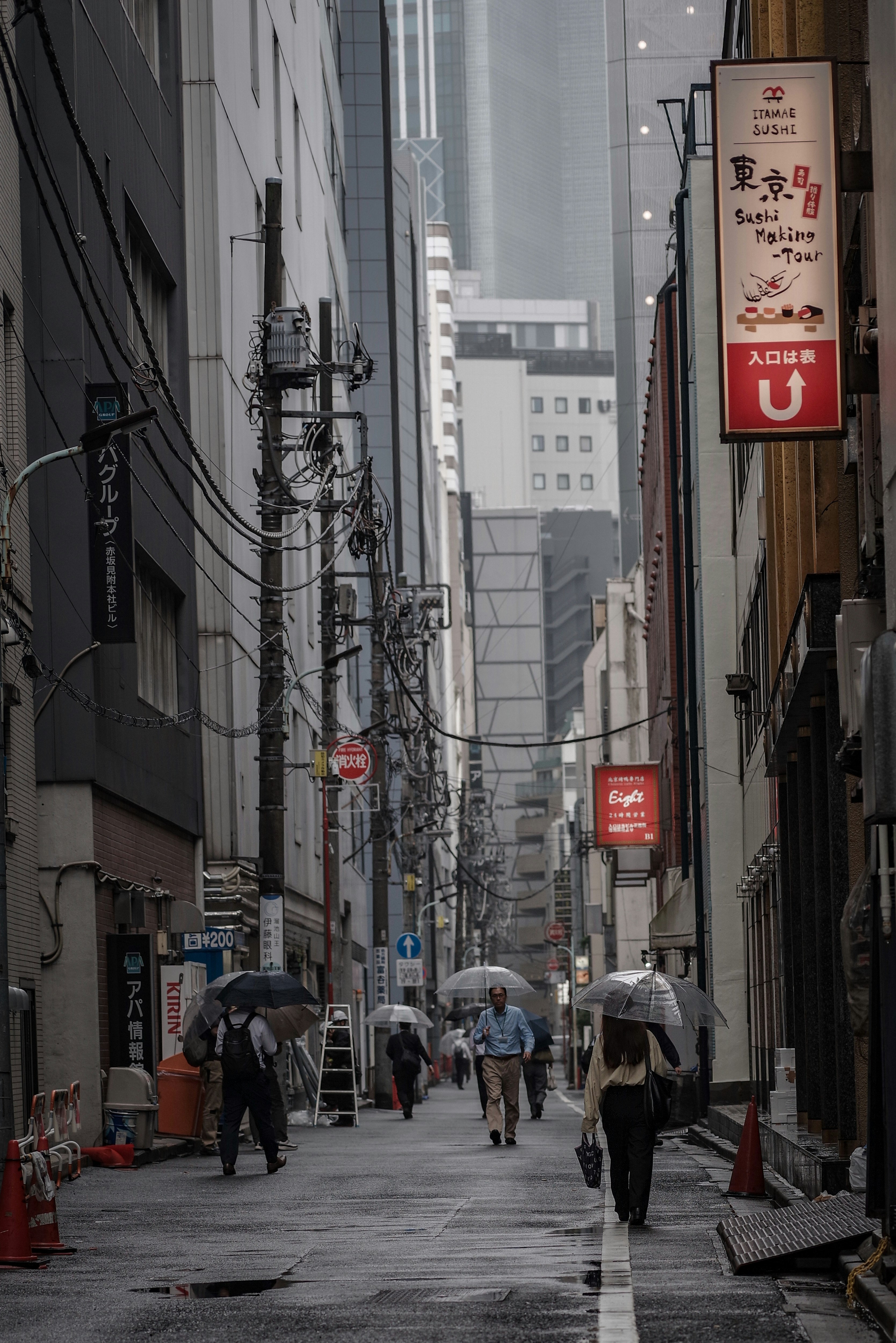 雨の路地を歩く人々と看板のある東京の街並み