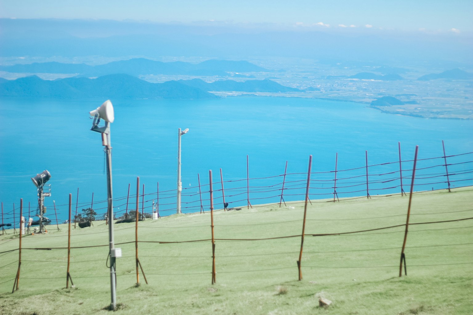 Vista panoramica di una collina che sovrasta un mare e un cielo blu con altoparlanti e pali visibili