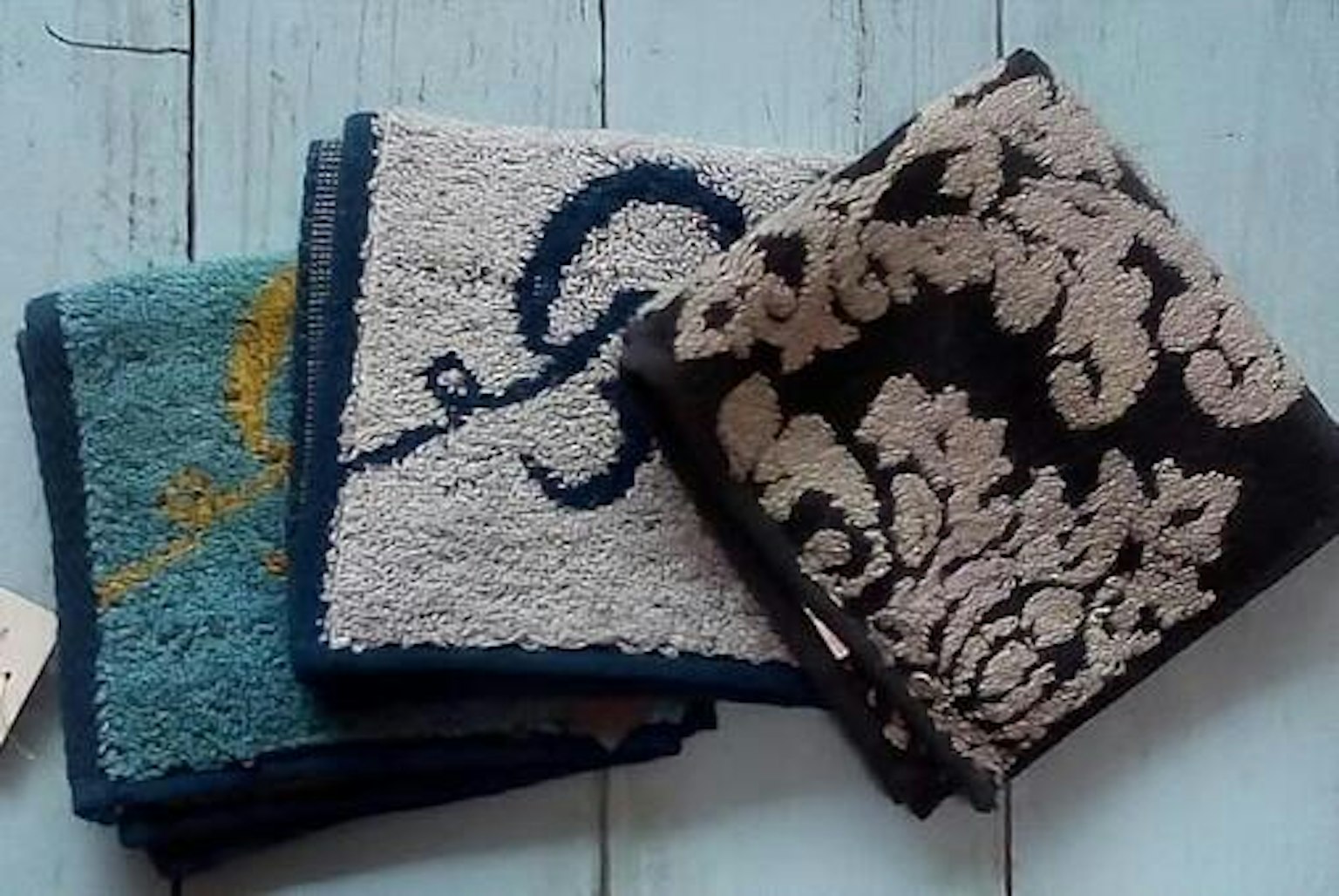 Tumpukan handuk berwarna-warni dengan handuk biru dengan desain kuning handuk putih dan handuk hitam dengan pola bunga