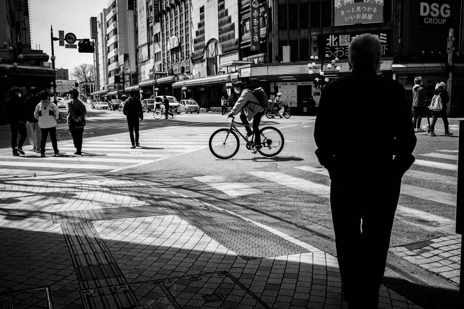 Una escena de calle en blanco y negro con un ciclista y peatones