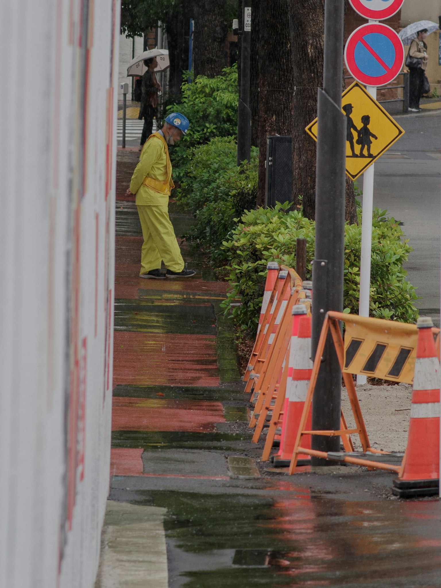 A worker in yellow rain gear standing on a wet sidewalk with traffic signs