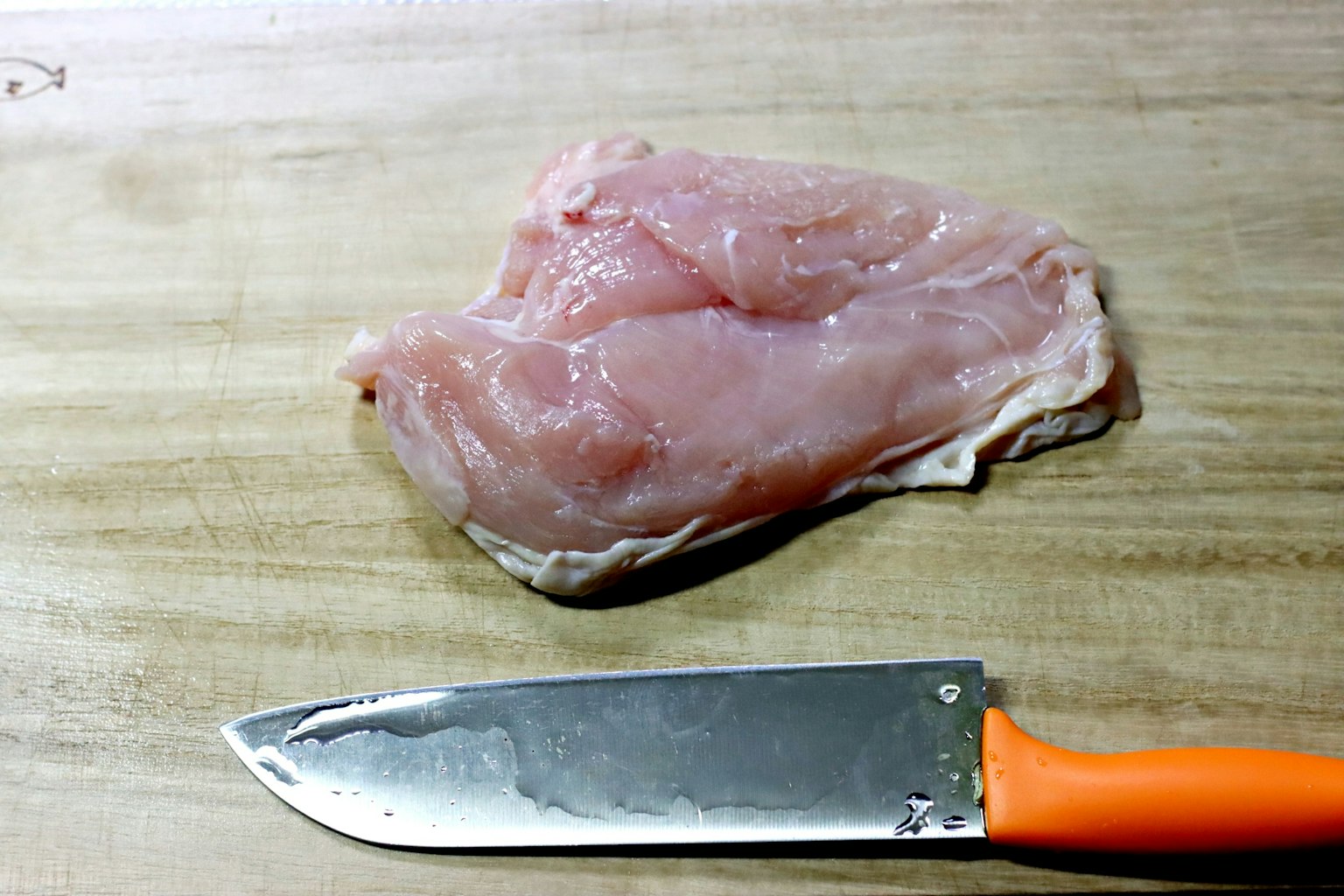木砧板上的生鸡肉和一把橙色手柄的刀