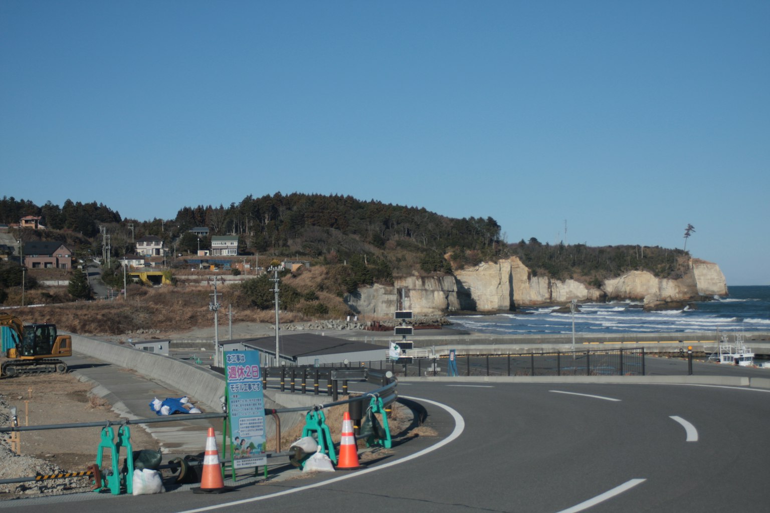 Strada costiera con cantiere e scogliere sullo sfondo