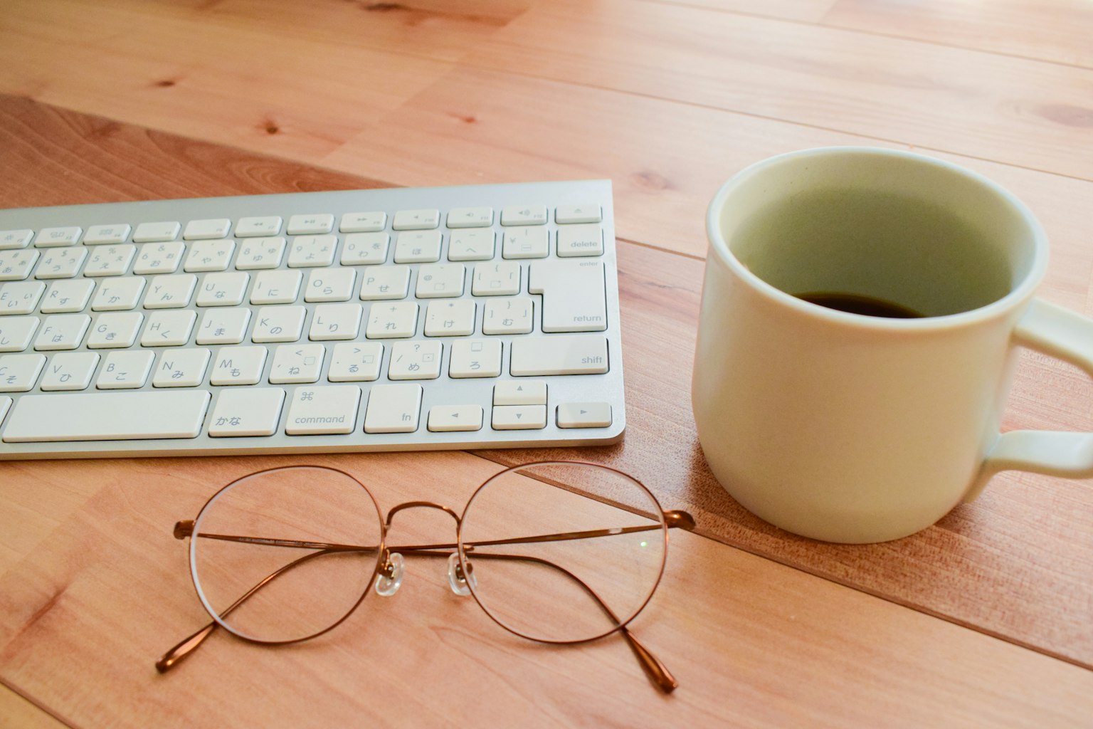 Eine Tastatur neben einer Kaffeetasse und Brille auf einem Holztisch