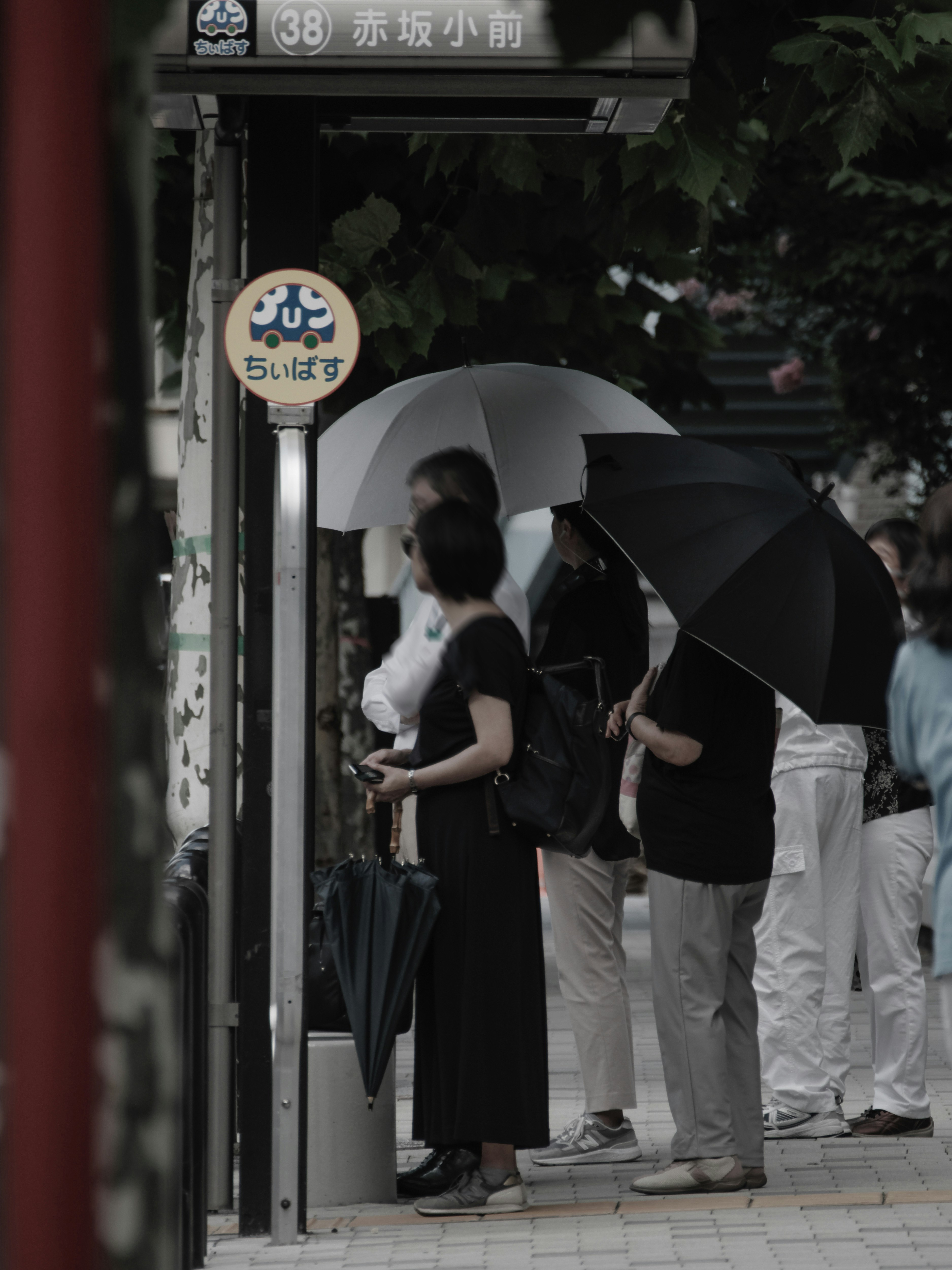 東京のバス停で傘を持つ人々のある街並み