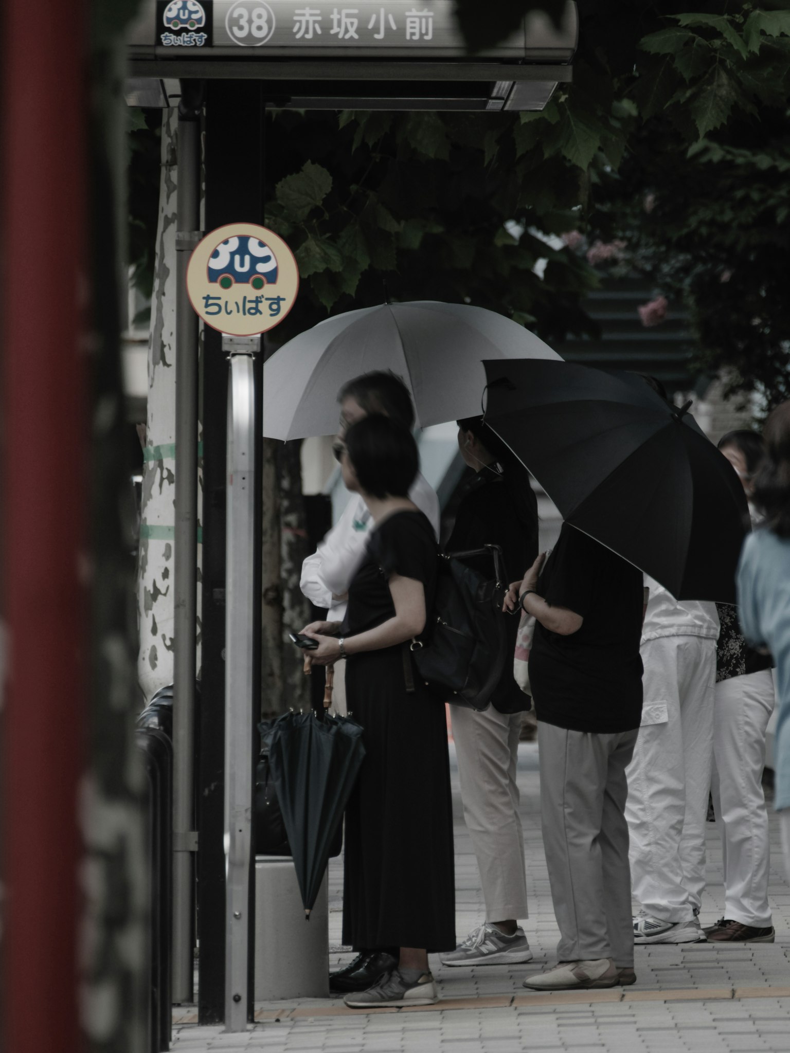 手持雨伞的人们在公交车站等候