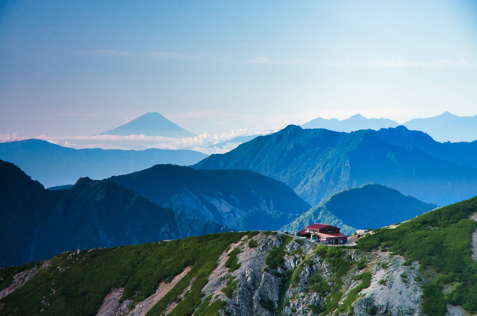 Vue panoramique de montagnes bleues avec une cabane rouge et le mont Fuji au loin