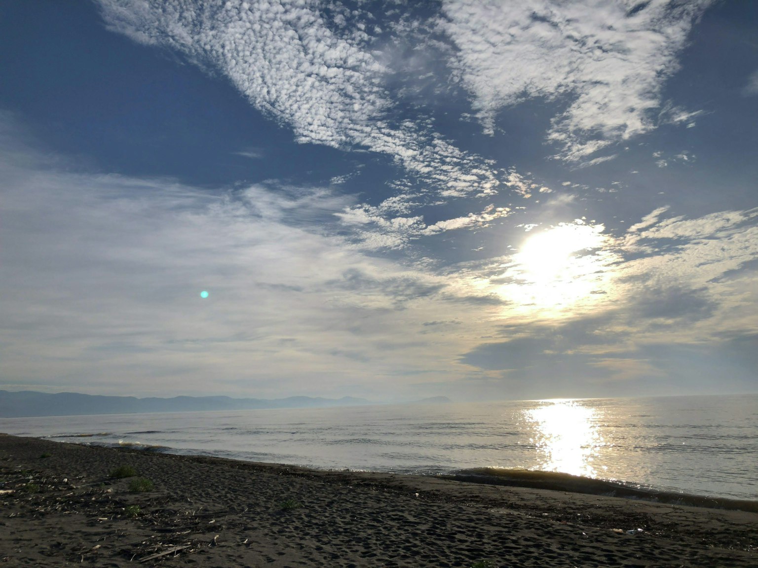 Pemandangan laut yang indah dengan awan dan cahaya matahari yang memantul di atas air tenang