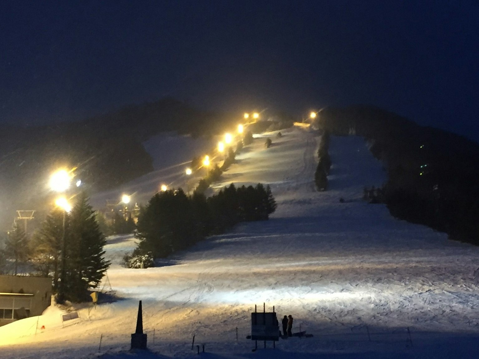 Vista nocturna de una pista de esquí cubierta de nieve con caminos iluminados
