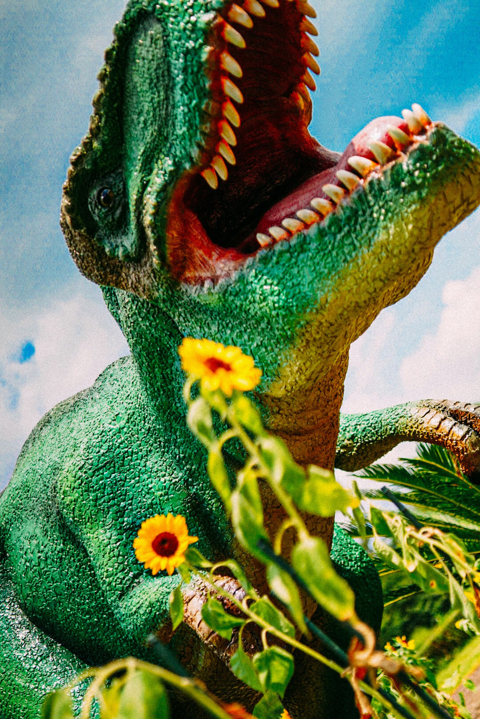 A green dinosaur standing among flowers with its mouth open