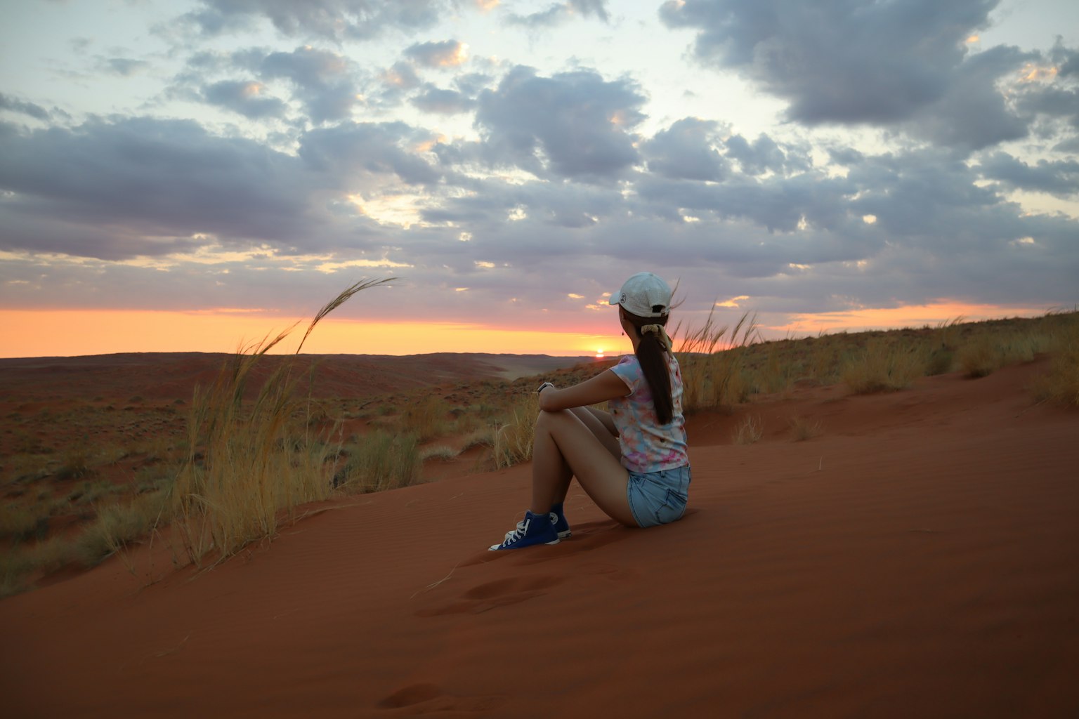 Une femme assise sur une dune de sable au coucher du soleil