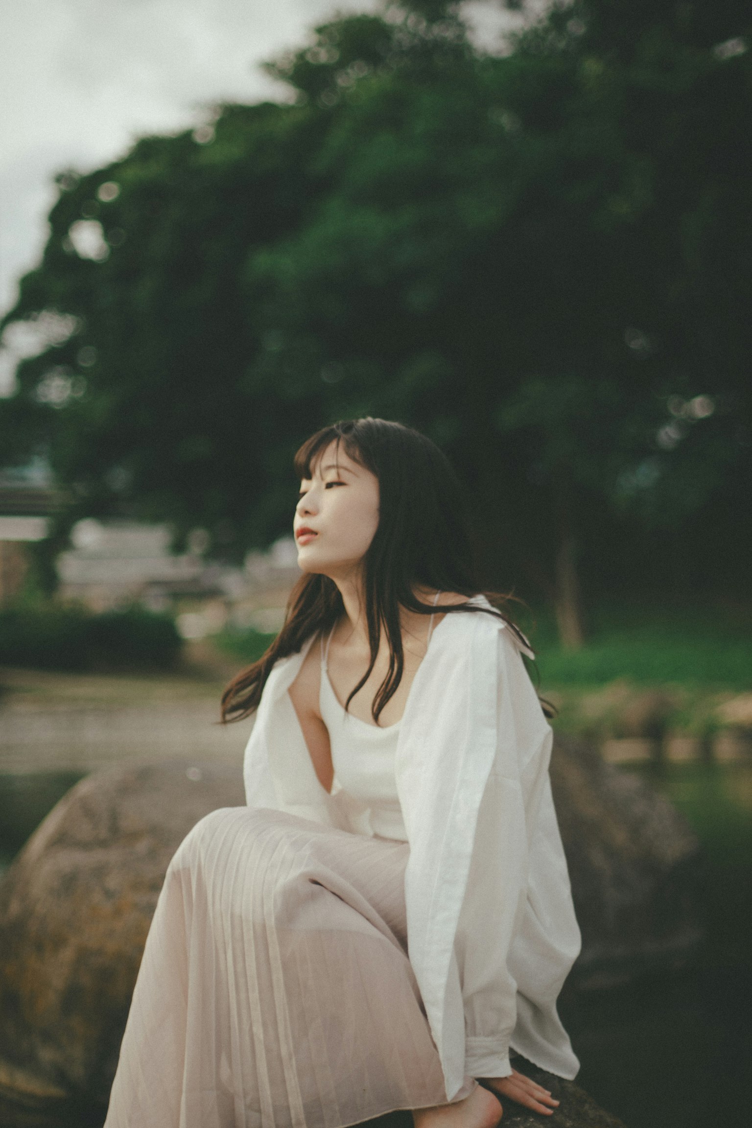 一位穿著白色上衣和輕薄裙子的女性坐在戶外的自然環境中