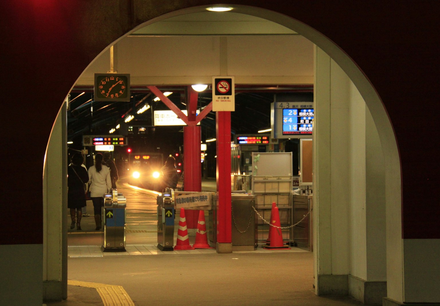 Bogenförmiger Eingang zu einem Bahnhof bei Nacht mit sichtbarer Uhr und Beschilderung