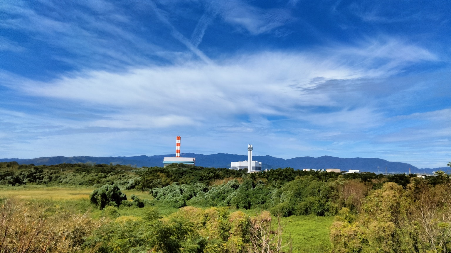 Estructuras de fábrica bajo un cielo azul con nubes blancas y paisaje verde
