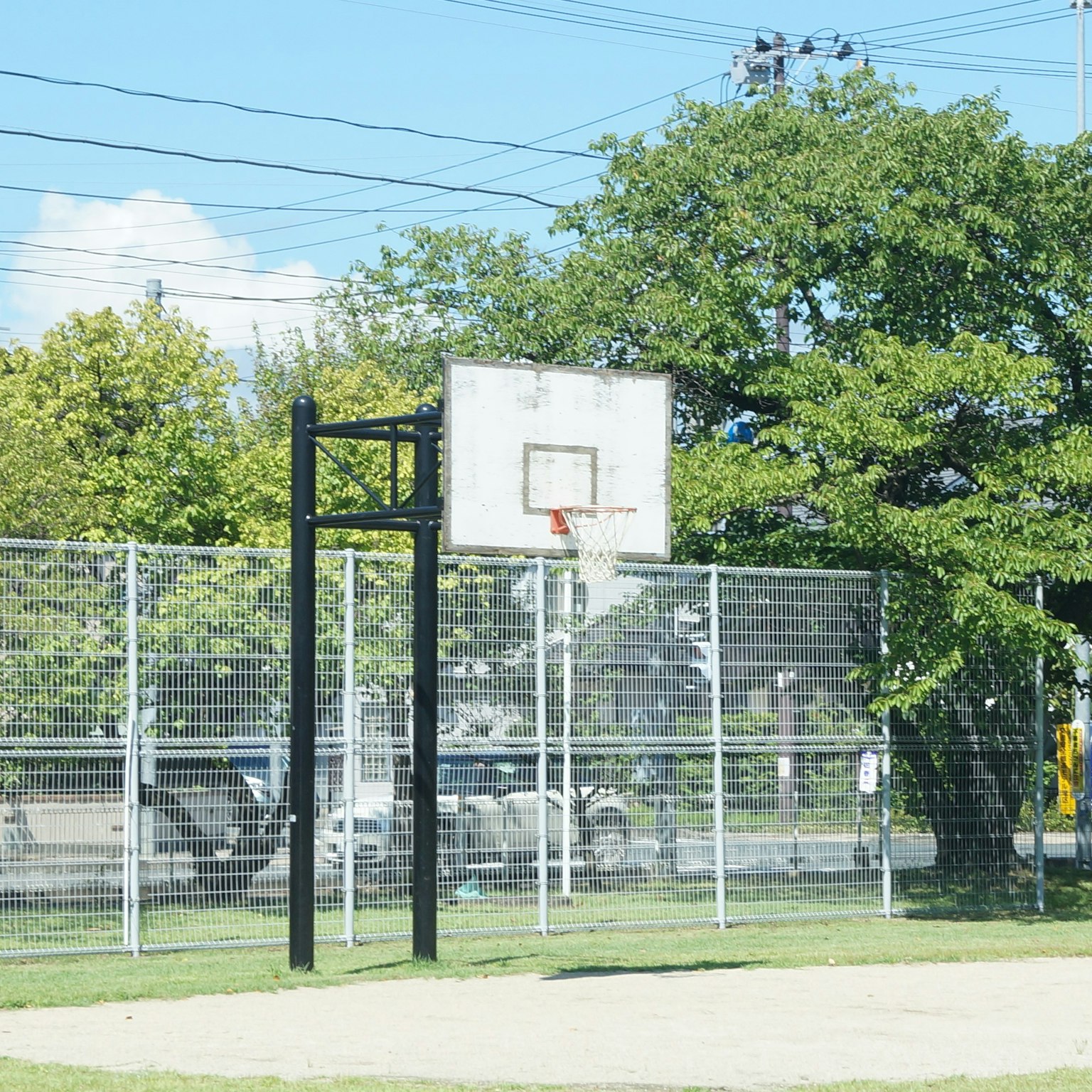 Panier de basket et clôture dans un parc sous un ciel bleu