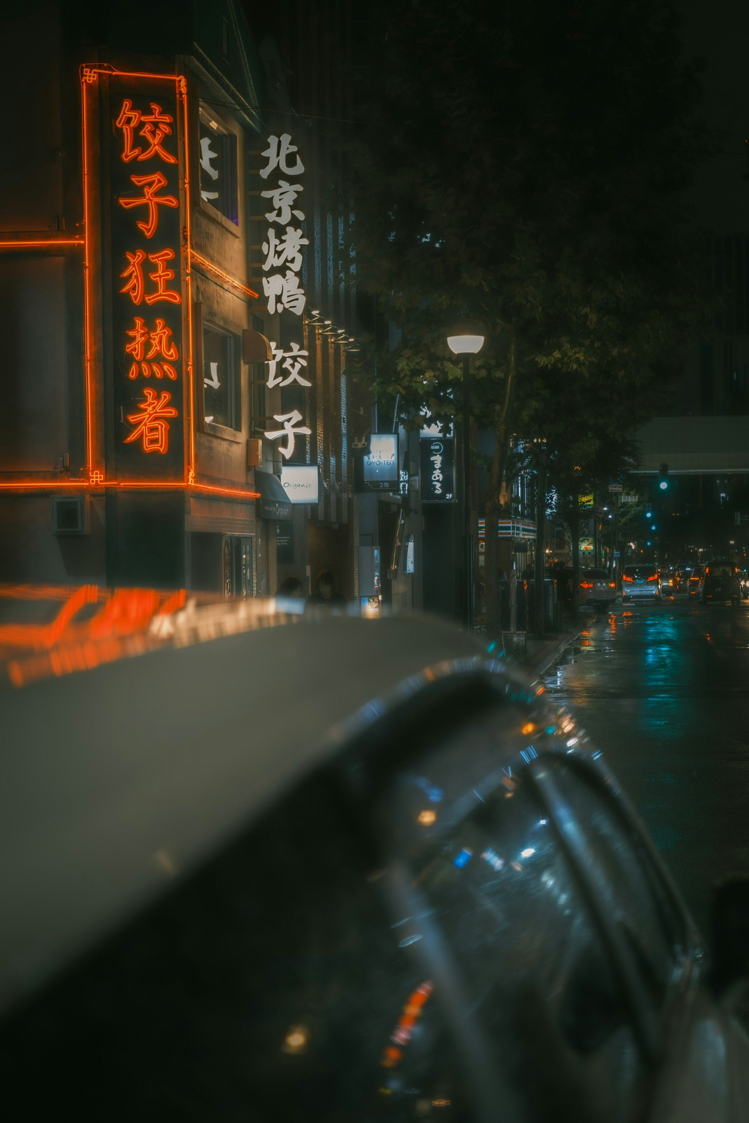 夜の街並みにある餃子店のネオン看板と雨に濡れた道路