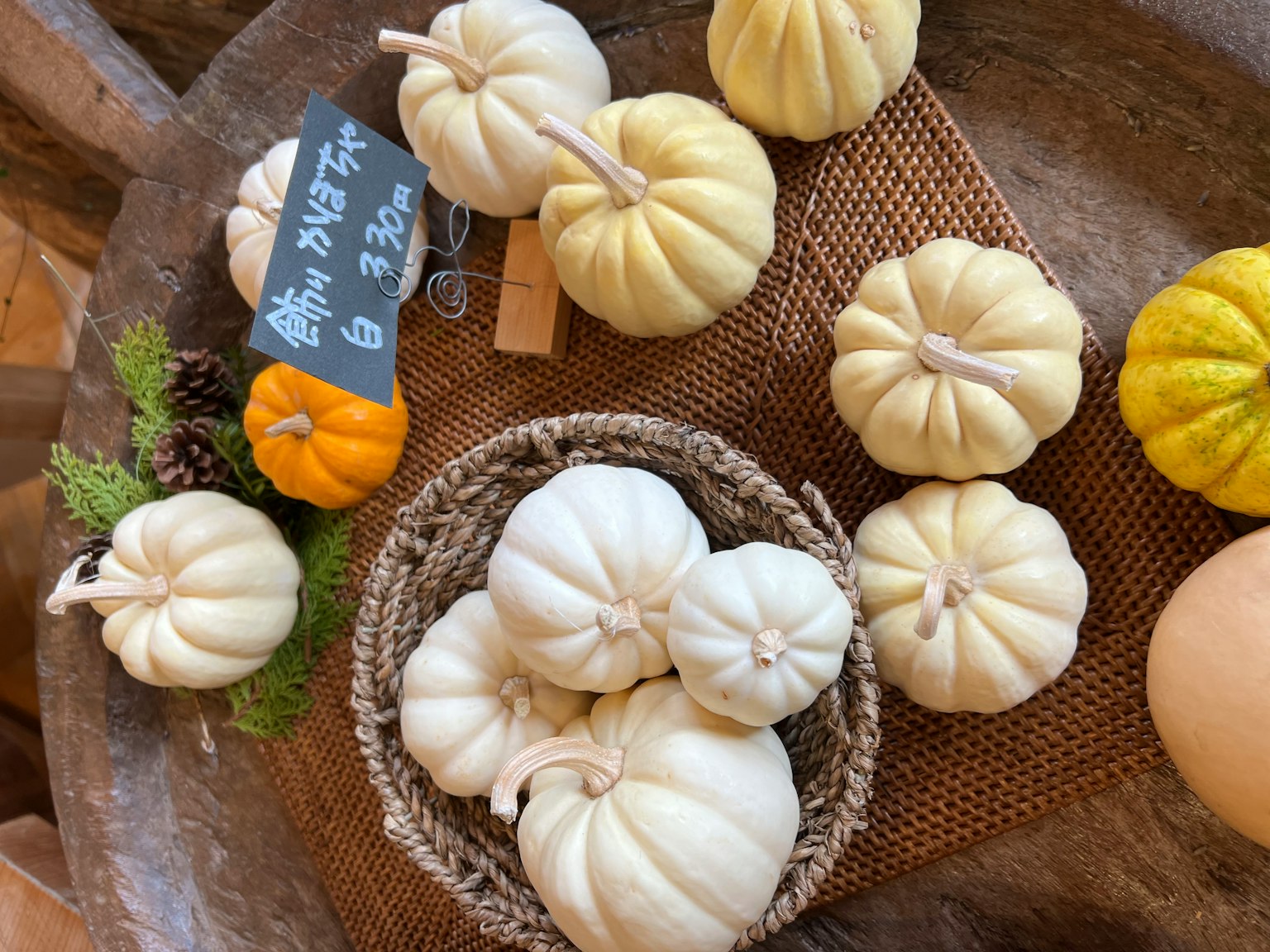 Scena di zucche bianche disposte su un tavolo cesto con zucche e una piccola zucca arancione alcune foglie verdi e un appunto su una lavagna nera
