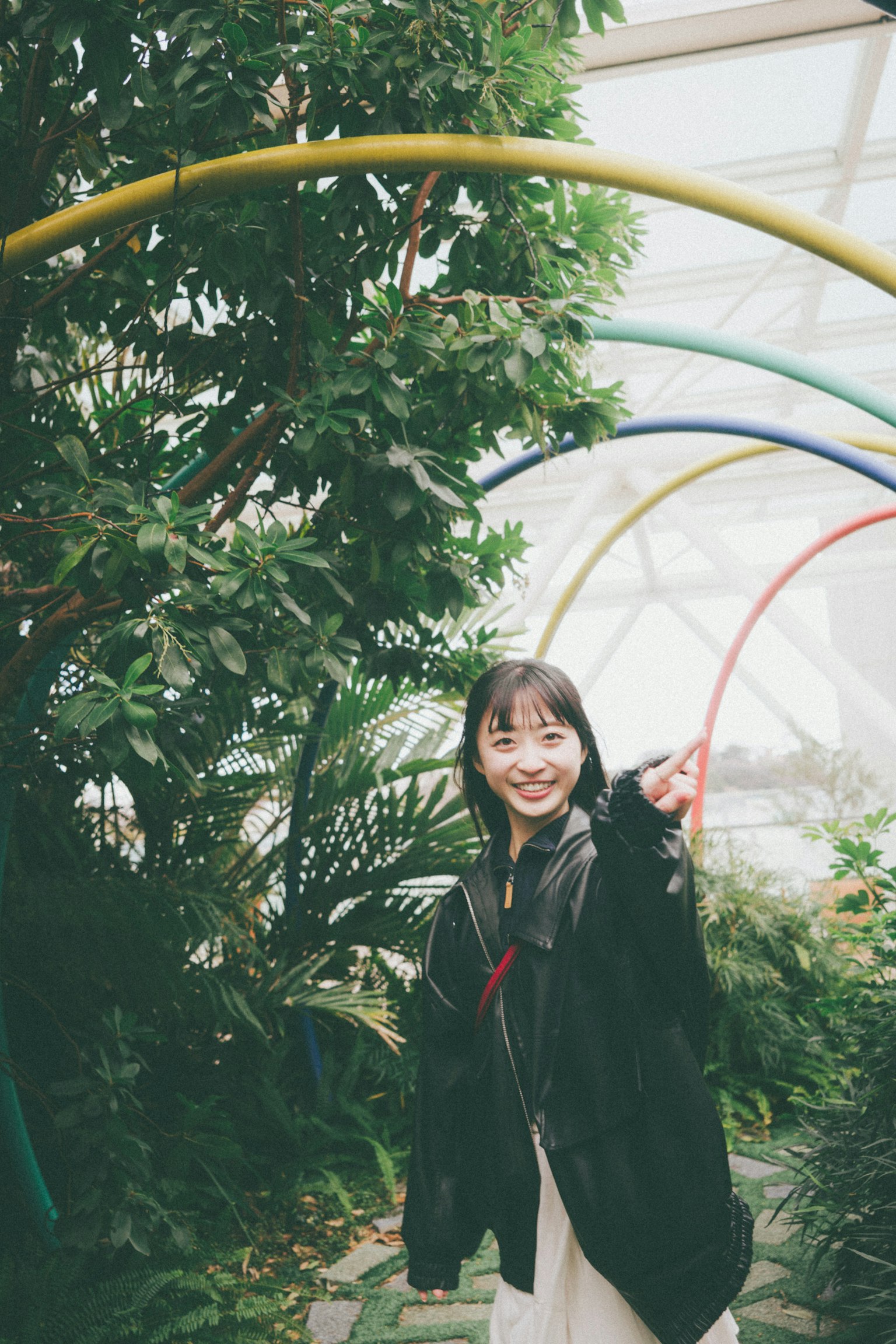 Donna sorridente che punta in un arco colorato circondato da piante verdi