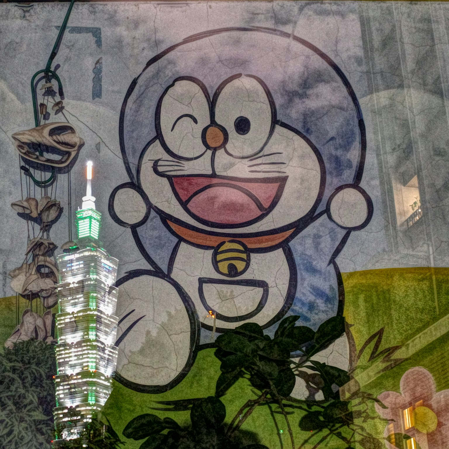 台北101の前に描かれたドラえもんの壁画 笑顔で手を振るキャラクター 緑の植物が周囲に配置されている