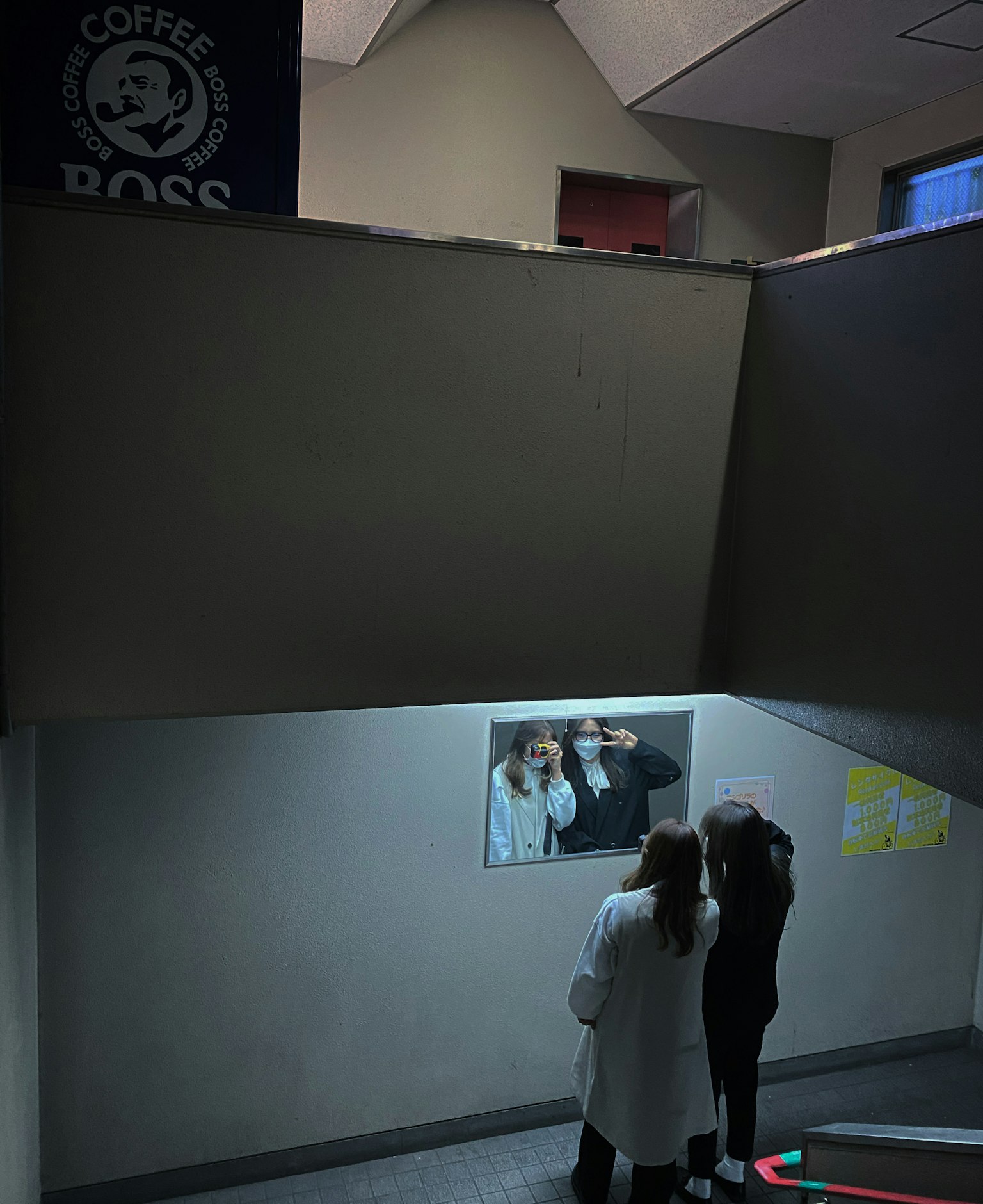 階段の下で写真を見ている二人の人物とコーヒーショップの看板