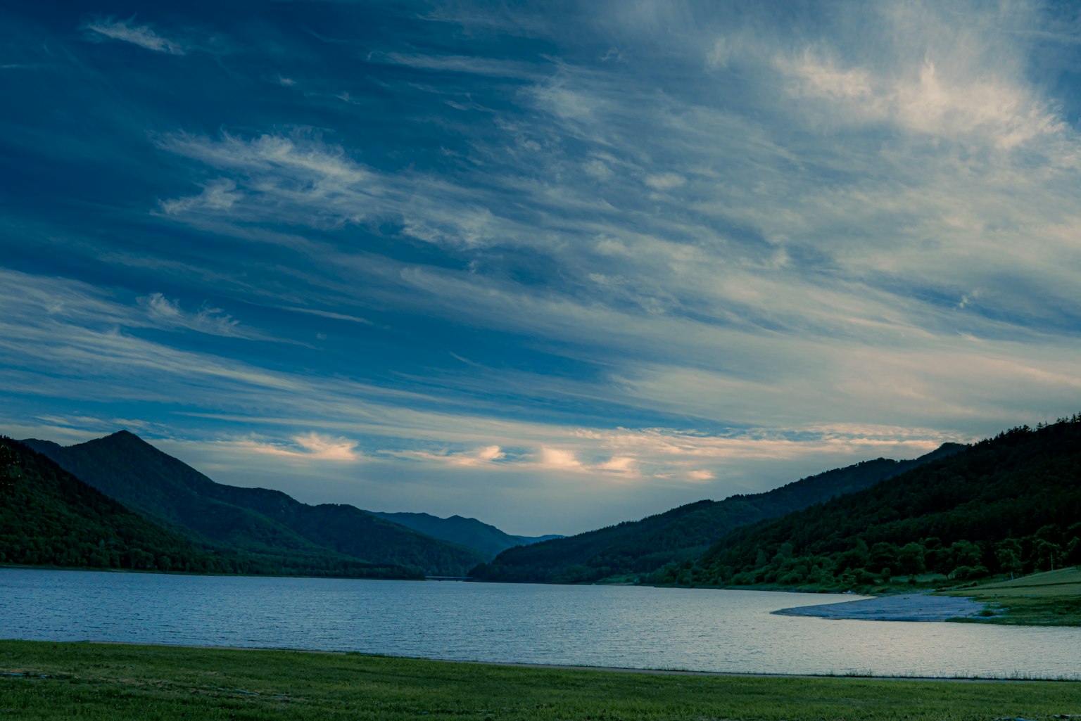 Scenic view of a blue lake surrounded by mountains under a cloudy sky