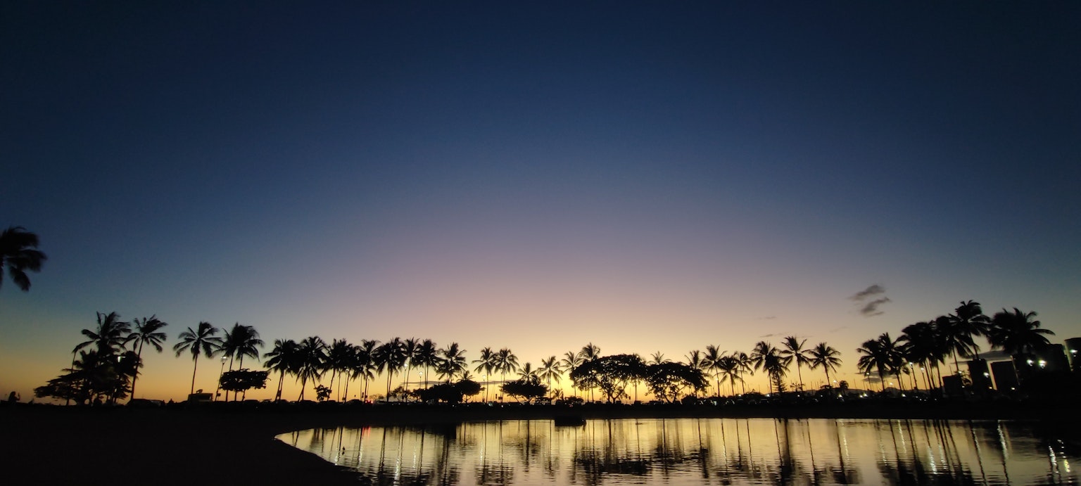 Agua serena reflejando un cielo al atardecer con palmeras en silueta